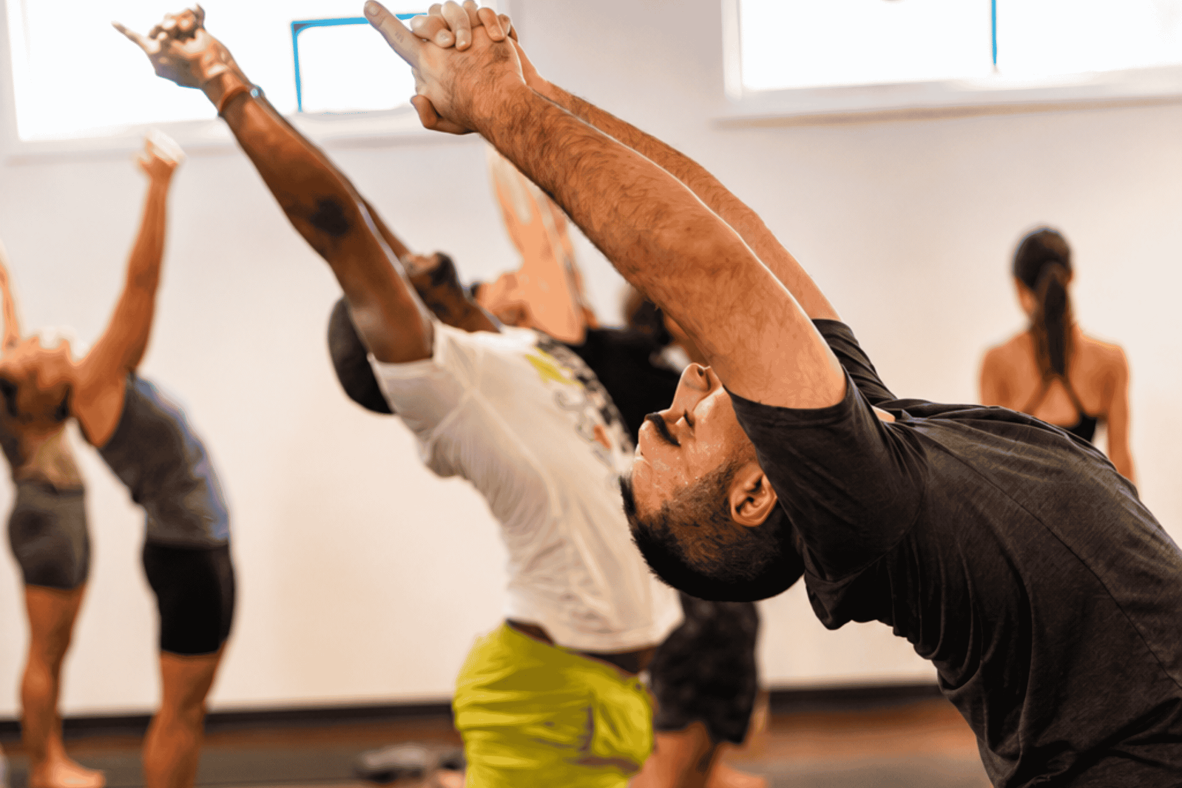 Hot yoga class leaning into a standing backbend with arms reaching overhead