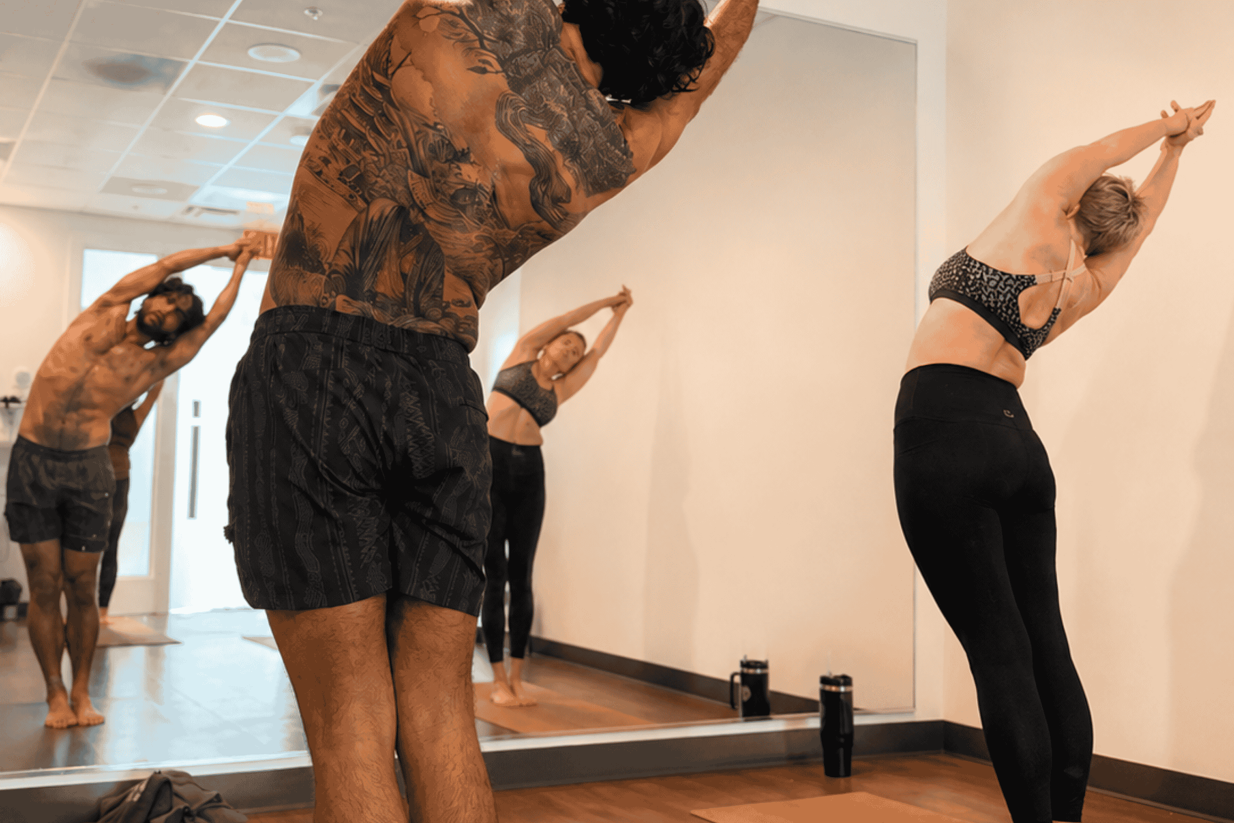 Class in a standing side bend with arms reaching overhead, reflected in the studio mirror