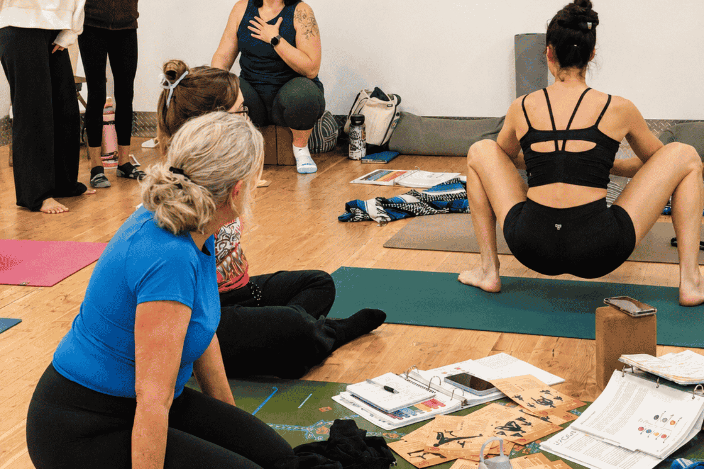 Yoga teacher trainees seated on mats with binders and notebooks spread around them