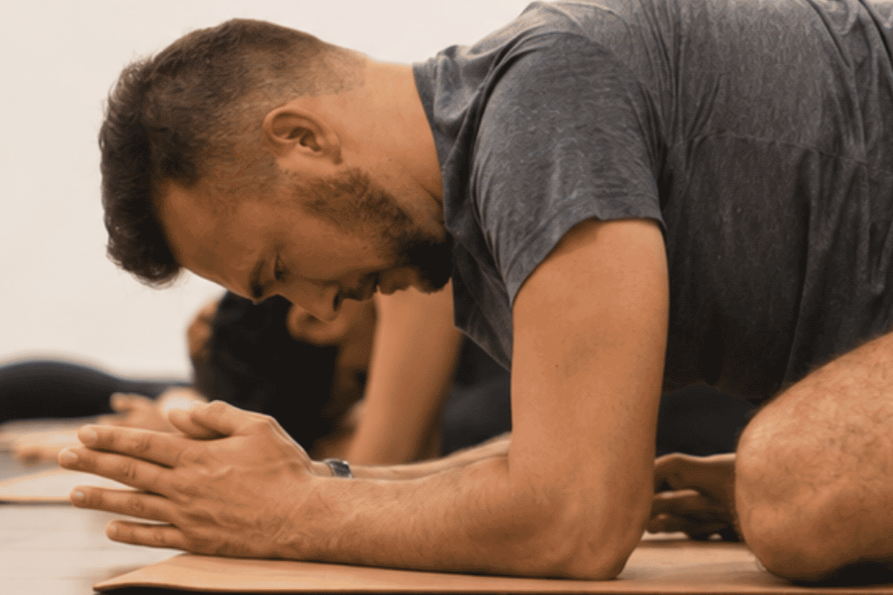 Person participating in a yoga or meditation class at yoga pod tucson, in a kneeling pose with hands pressed together in prayer position, head bowed.
