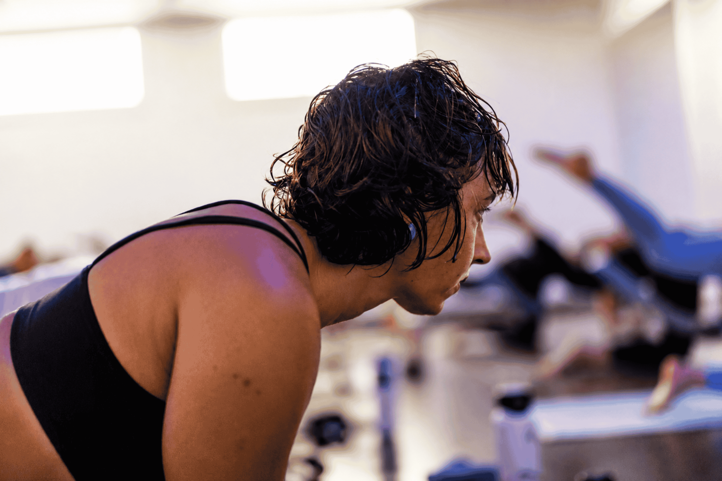 A woman with curly hair and a black athletic top focusing during a yoga pod tucson fitness class.