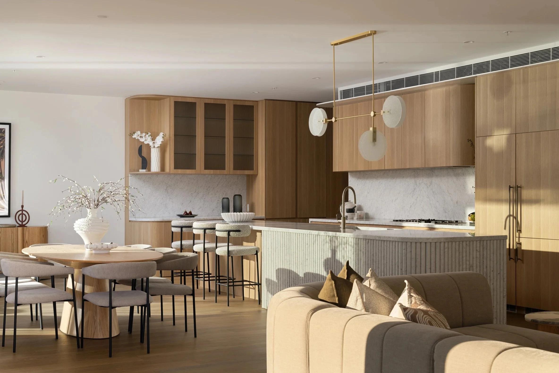 Modern open-concept kitchen and dining area with wood cabinetry, a marble island, and a beige sofa with decorative pillows.