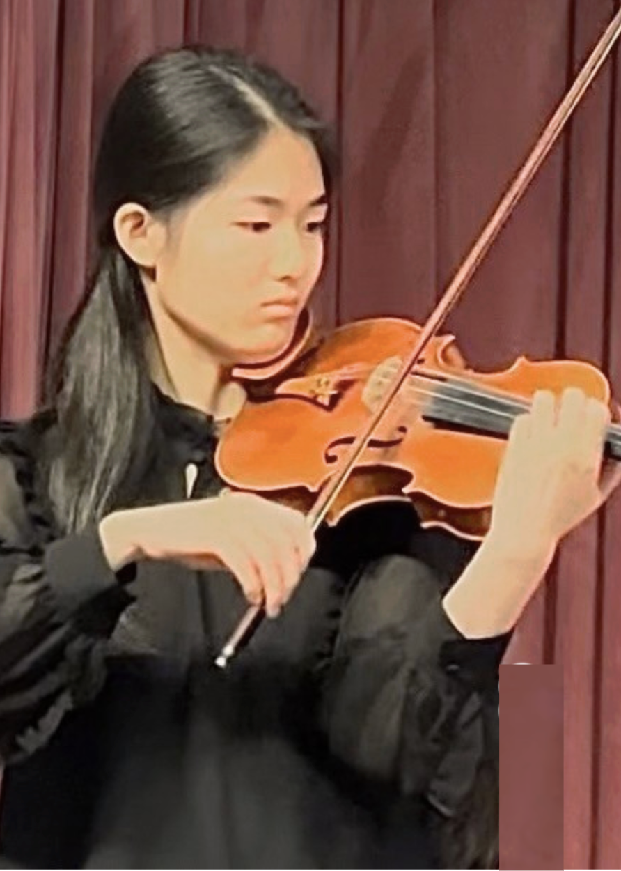 Young woman playing the violin in front of a maroon curtain
