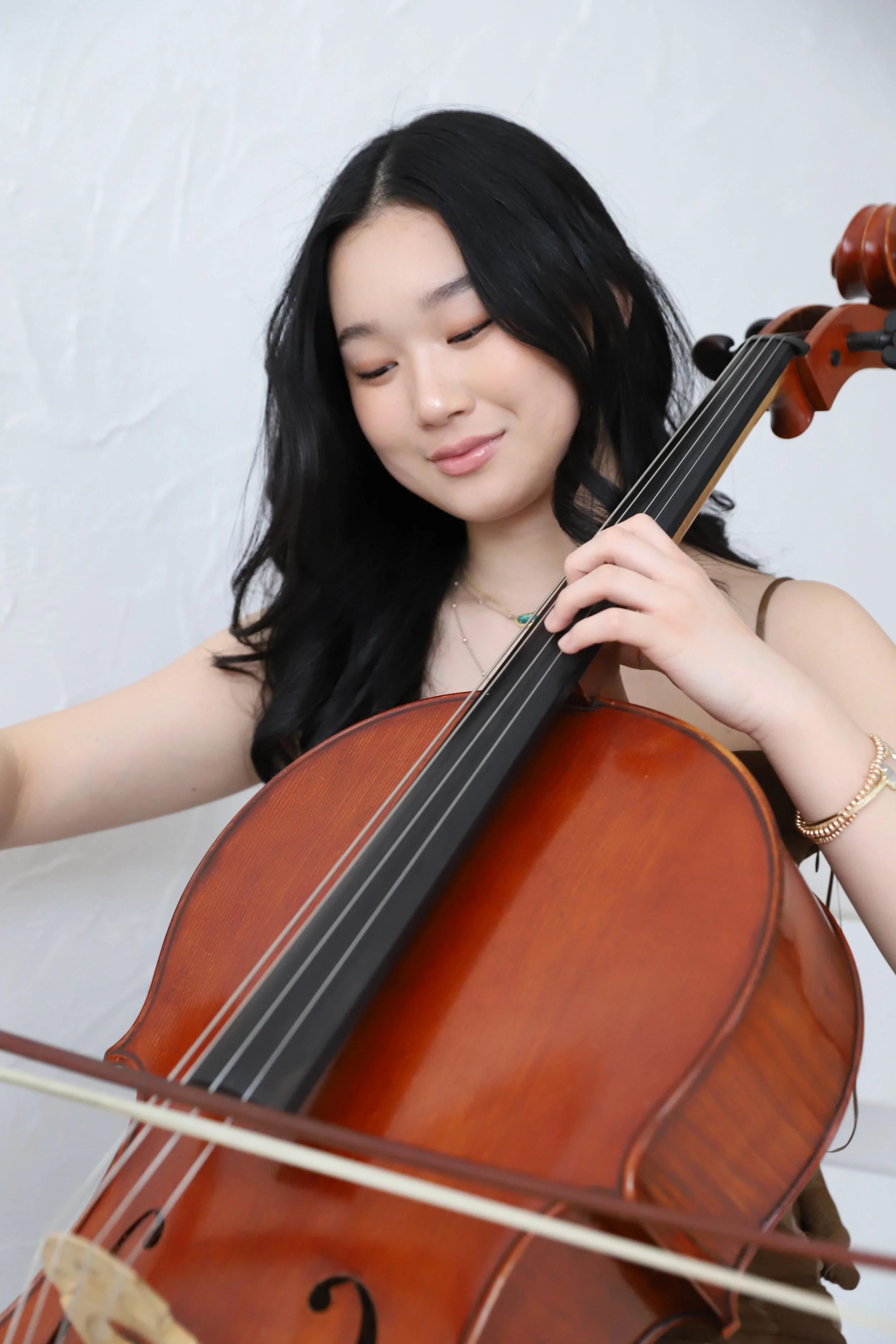 A young woman with black hair playing a violin, with a faint smile on her face against a plain white background.
