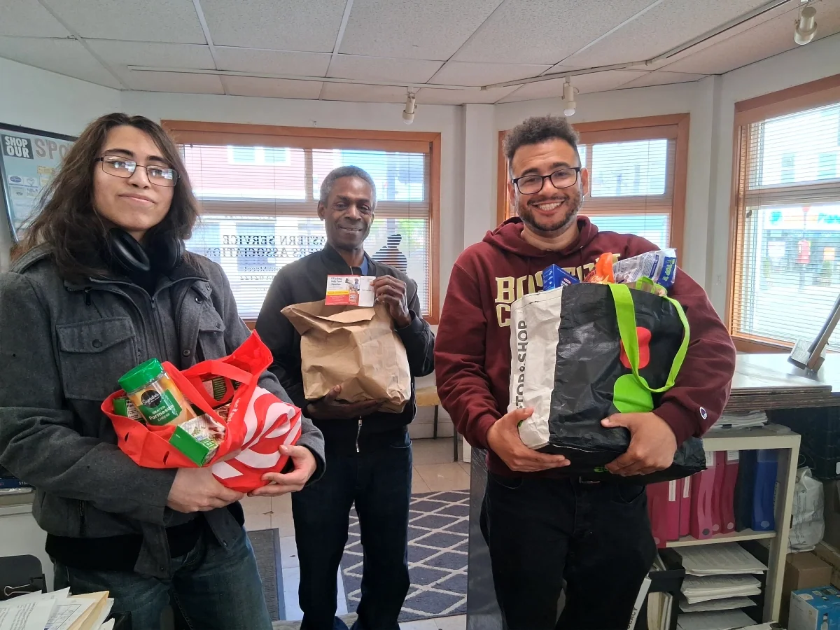 Photo of three volunteers smiling in the ESWA office each carrying a bag of donated food.