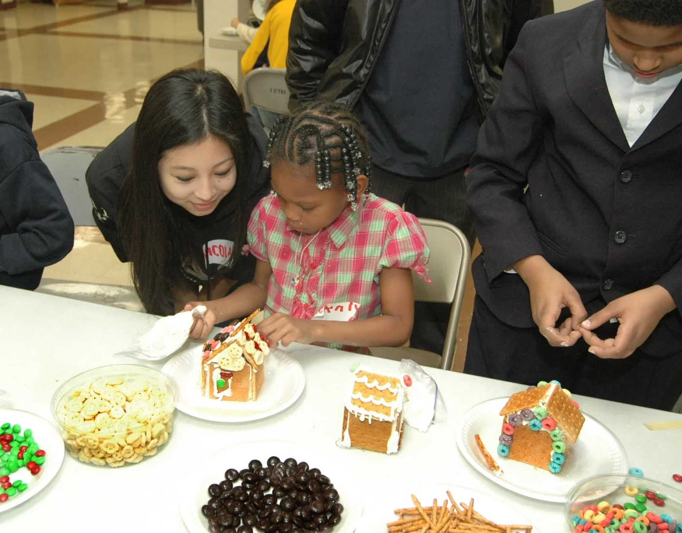 ESWA volunteer next to a girl building a gingerbread house.