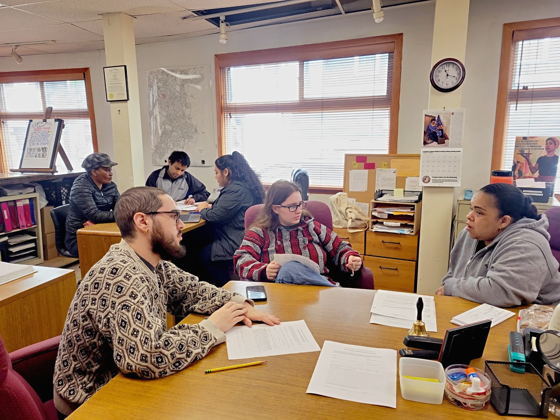 Photo of two groups of volunteers and members in the ESWA office, with one volunteer listening to the member and another volunteer taking notes in each group.