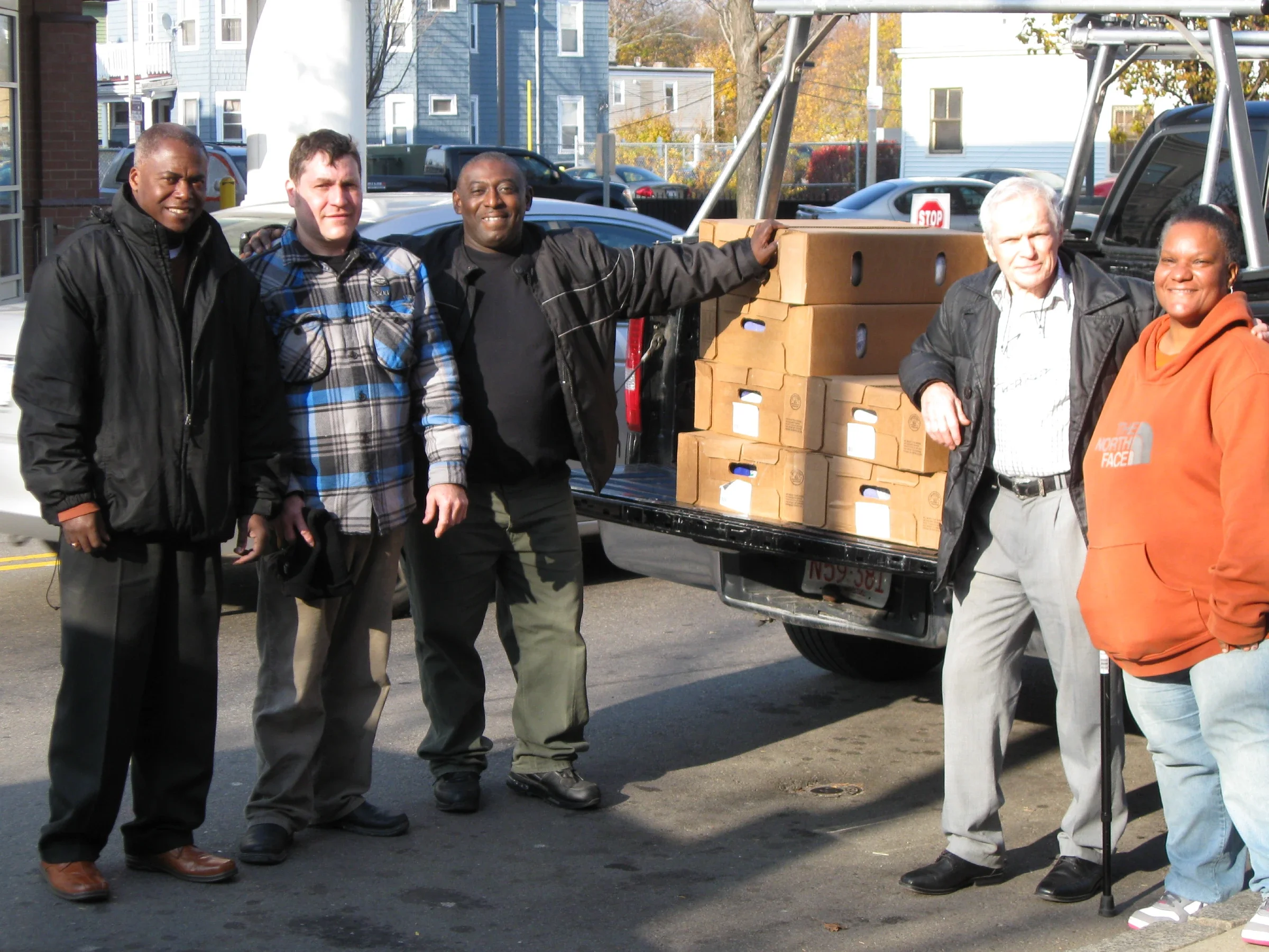 Smiling volunteers in winter coats standing by a truckbed filled with cases of donated food.