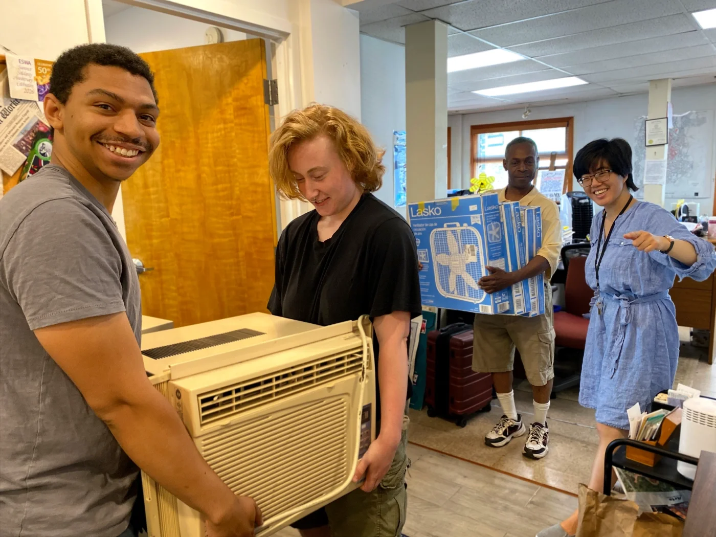 Smiling ESWA organizers and volunteers carrying an air conditioner unit and fans.