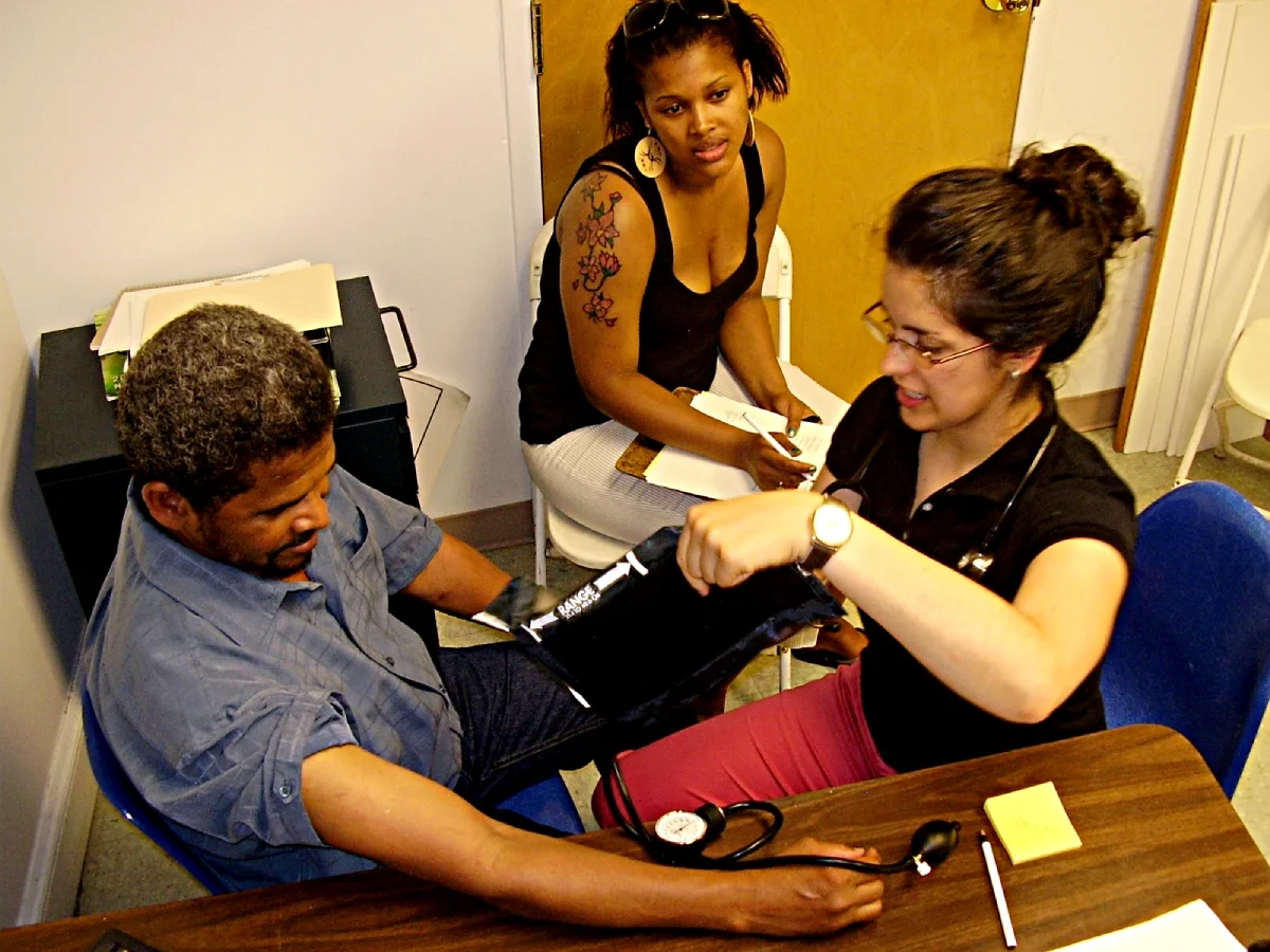Volunteer doctor checks an ESWA member's blood pressure as a volunteer advocate takes notes.