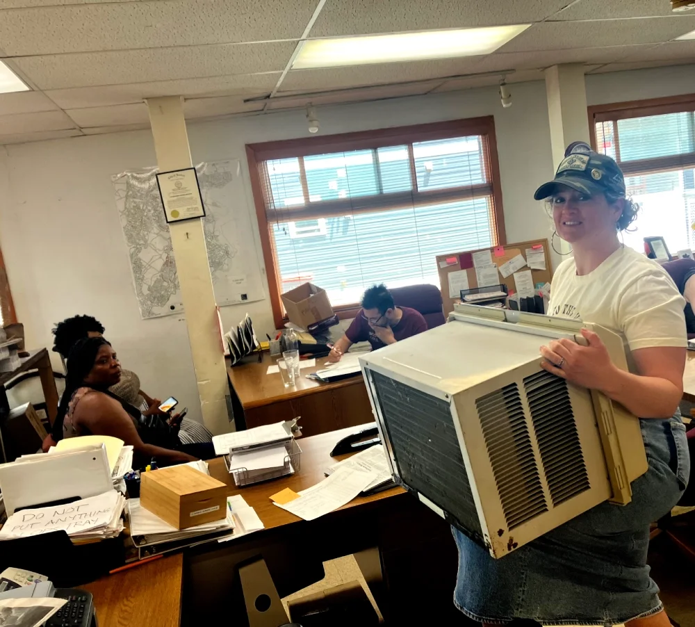 ESWA volunteer carrying an air conditioner unit while in the background another volunteer fills out a member's benefit request form.