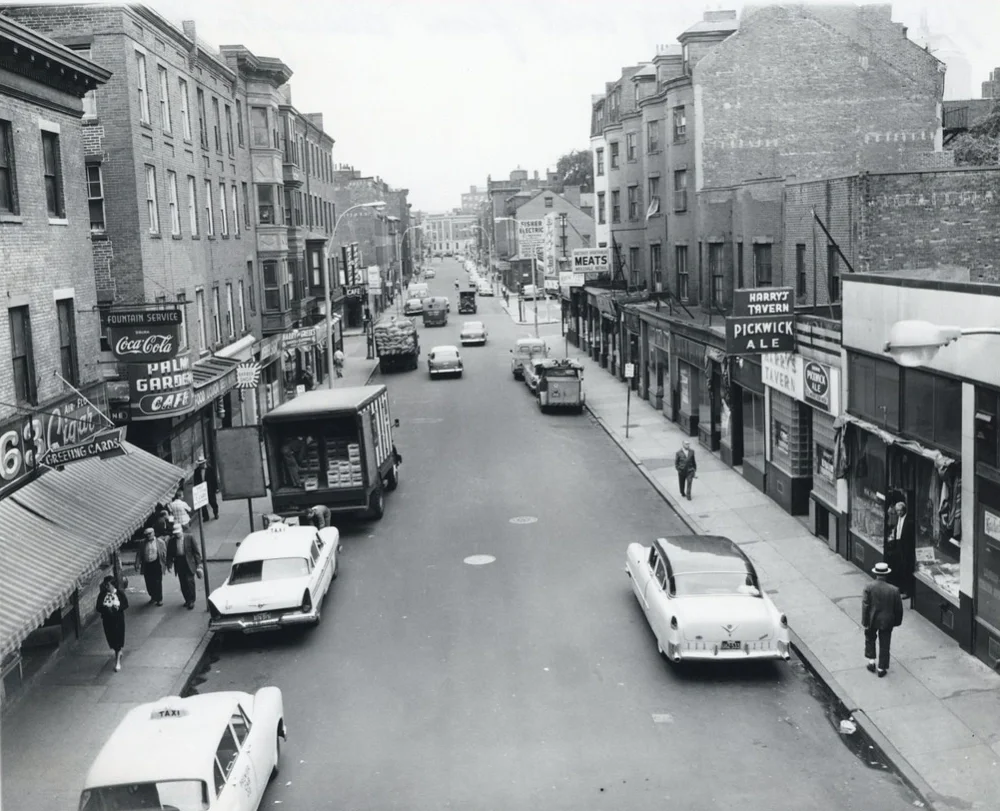 Black and white historic photo of a busy street lined with businesses.