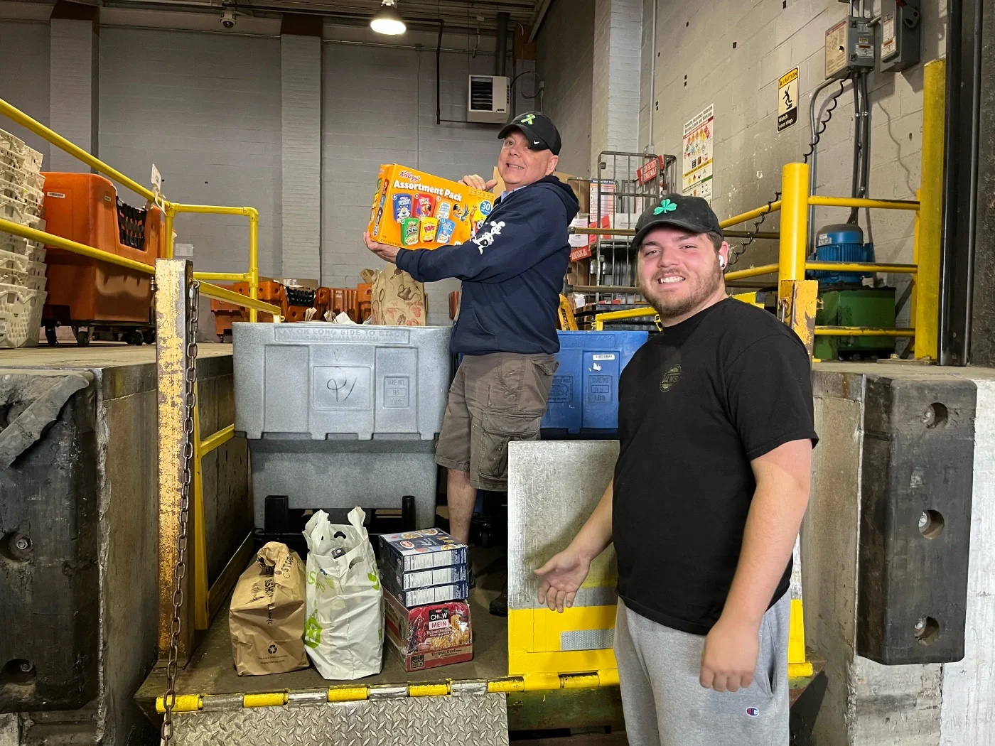 Two smiling postal workers standing with a truckload of donated food.