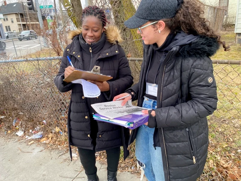ESWA volunteer standing with a binder next to a smiling woman signing up as an ESWA member.