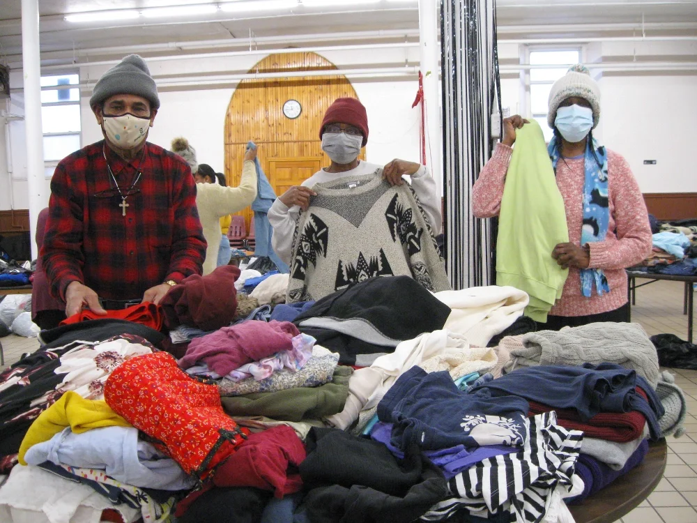 Volunteers behind a table covered in clothing holding up sweaters.