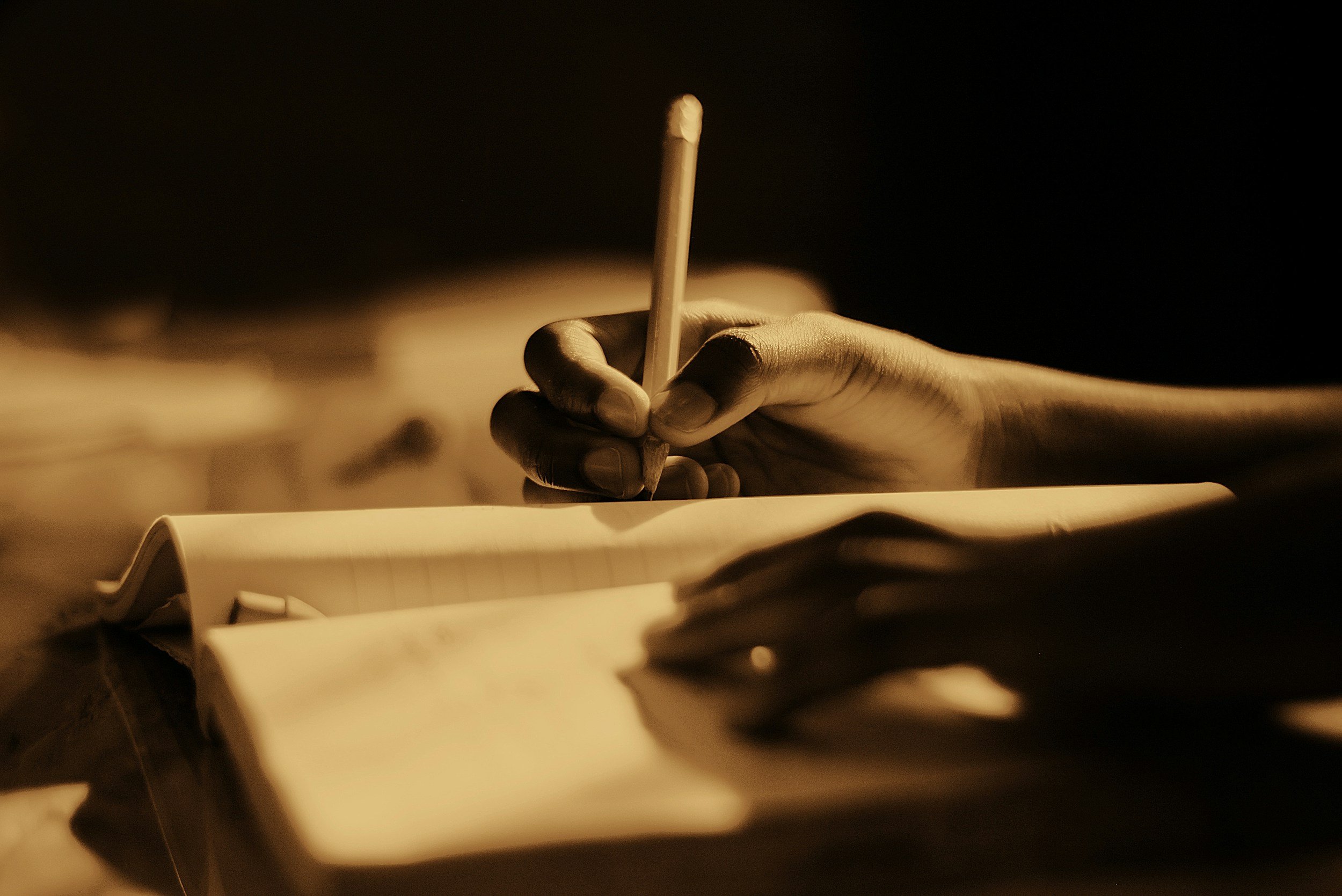 A hand holding a lit match over an open notepad in warm lighting.