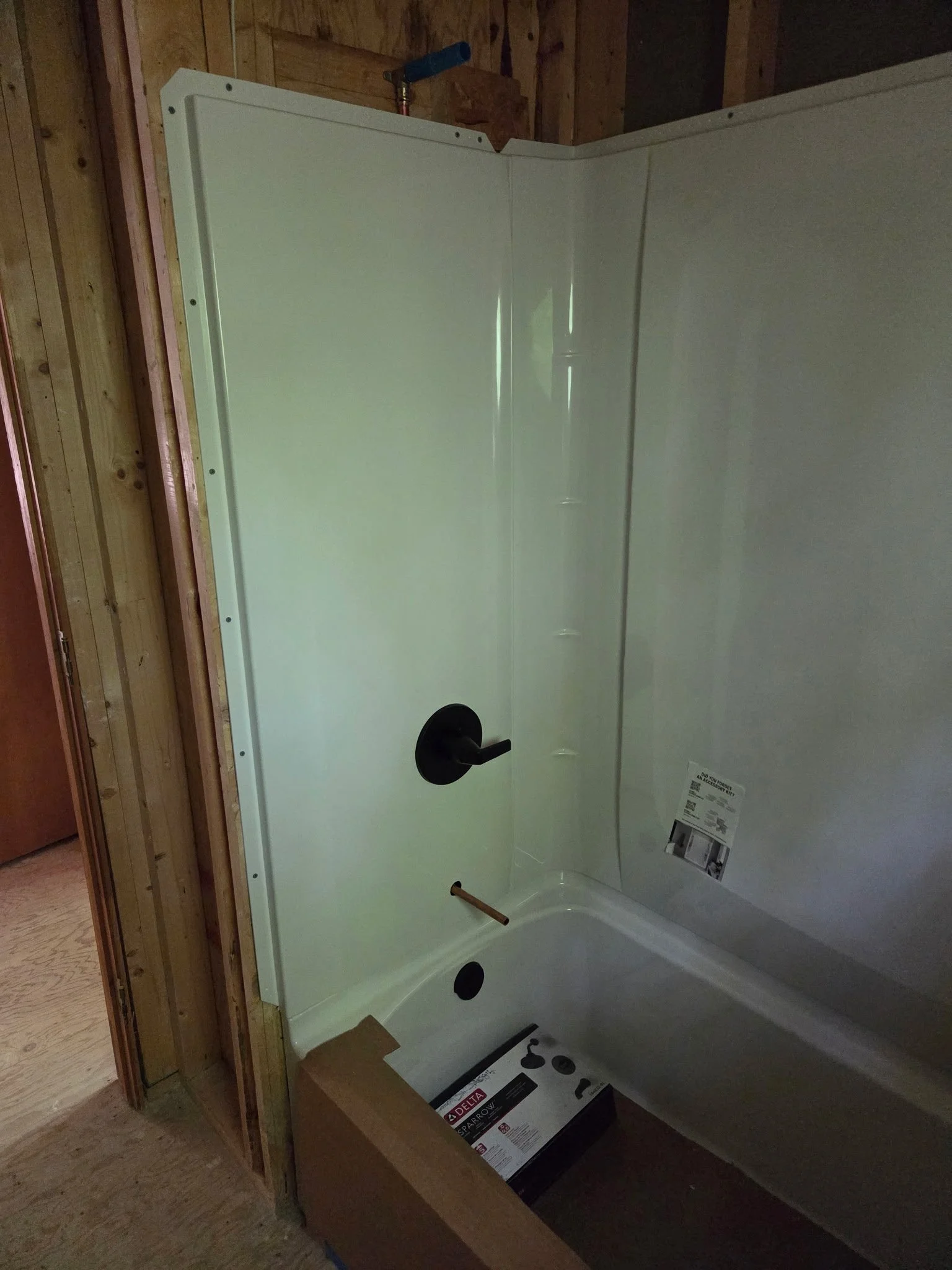 A new bathtub installed in an unfinished bathroom with exposed wooden wall frame and construction materials nearby.