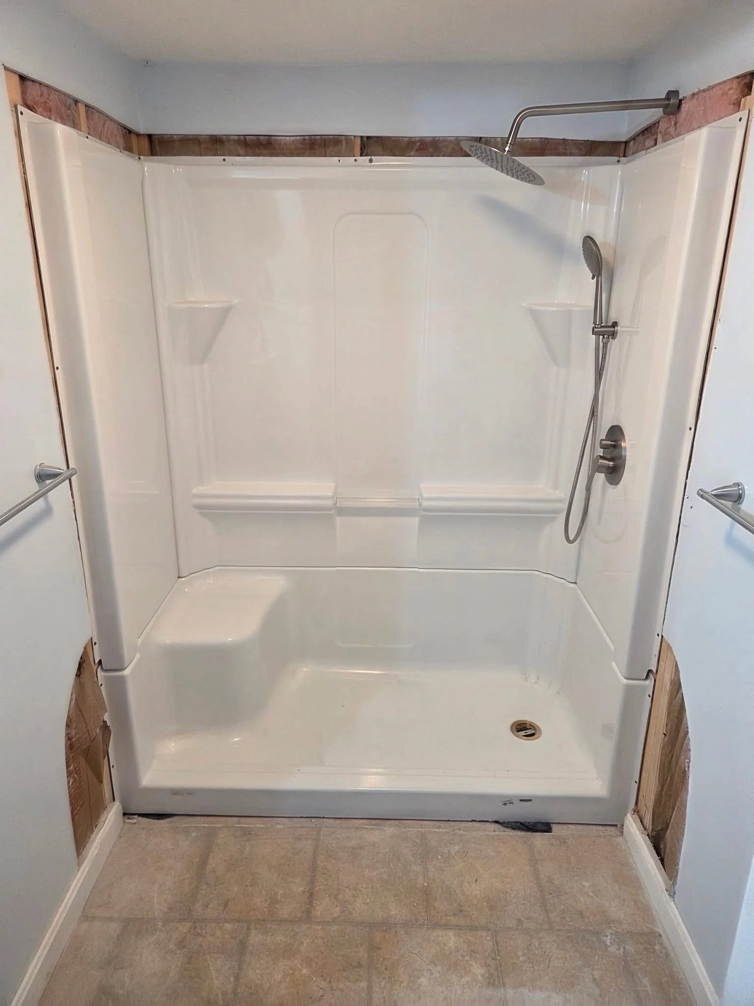 Bathroom shower area with a white shower base, a showerhead, and a handheld shower wand, with unfinished wall areas at top and sides.