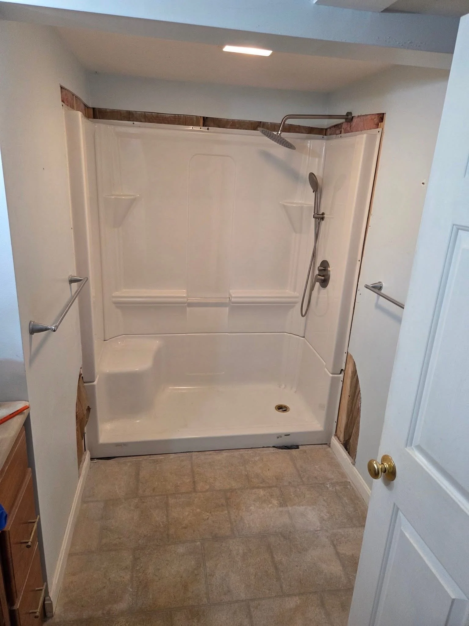 Bathroom with a white shower enclosure and two hanging towel bars, beige tiled floor, white door with a gold door handle.