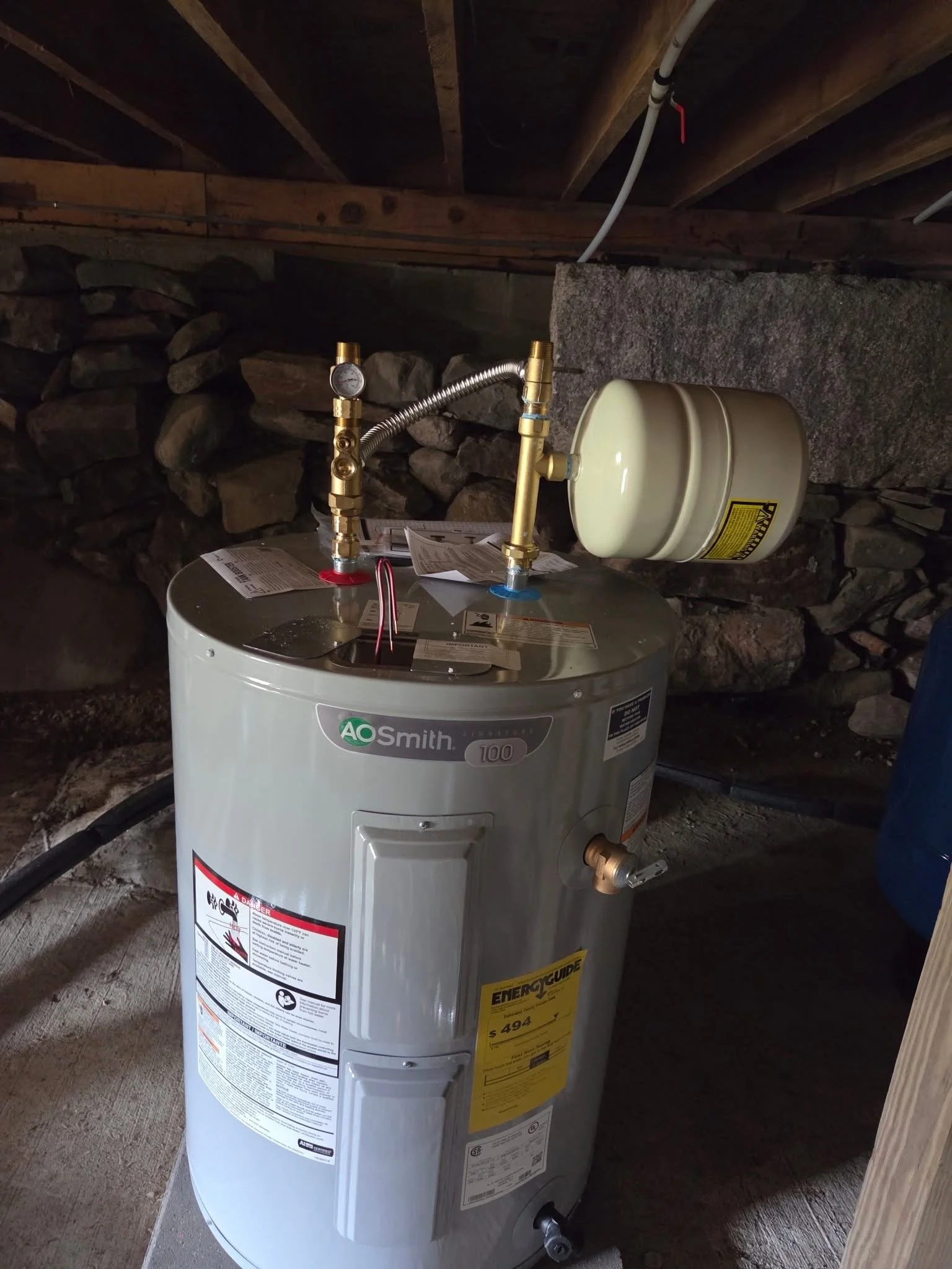A new water heater installed on a concrete floor in a basement or utility room, with pipes and wiring connected.