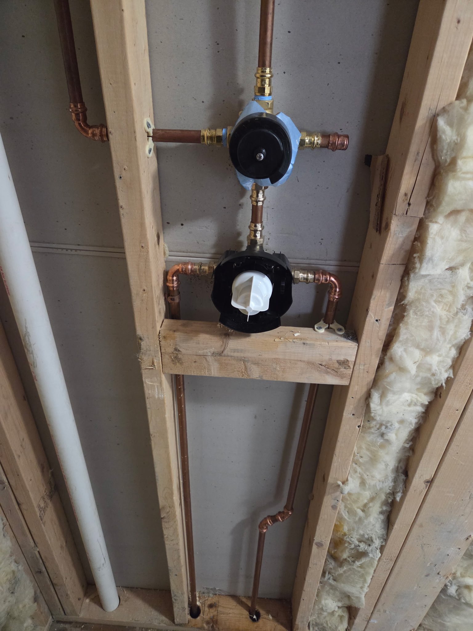 Plumbing pipes and components installed in a wall frame with insulation on one side.