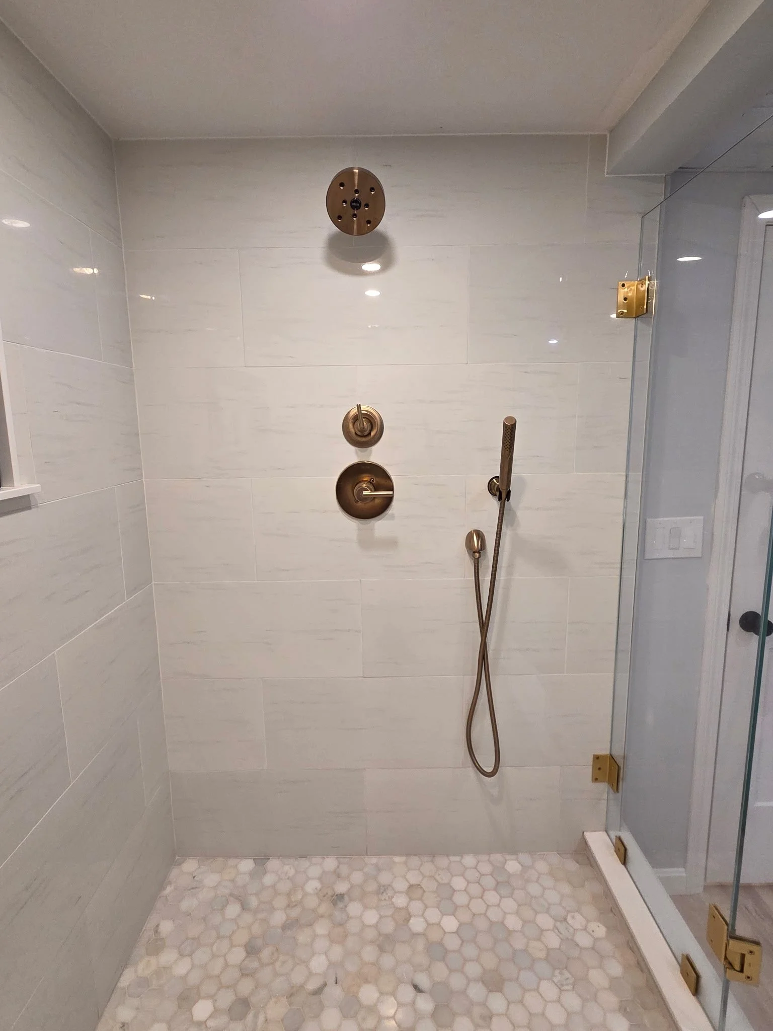 Shower with brass fixtures, glass door, and small hexagonal tile floor in a modern bathroom.
