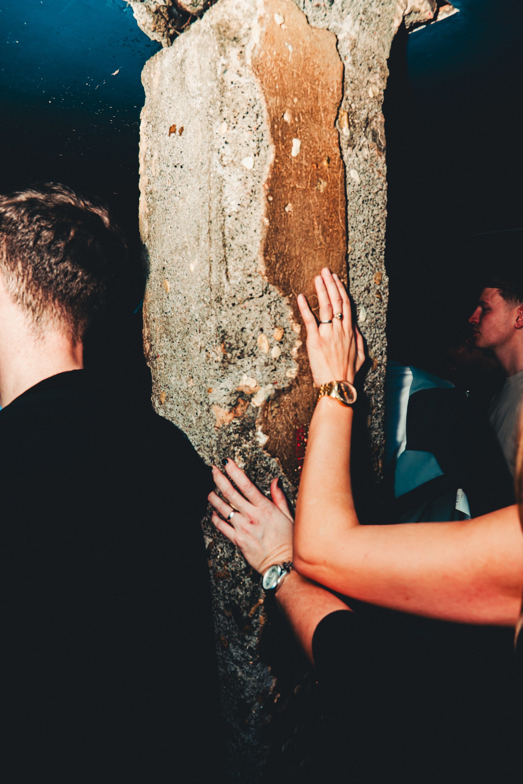 People touching a large stone with a biblical passage engraved on it near water