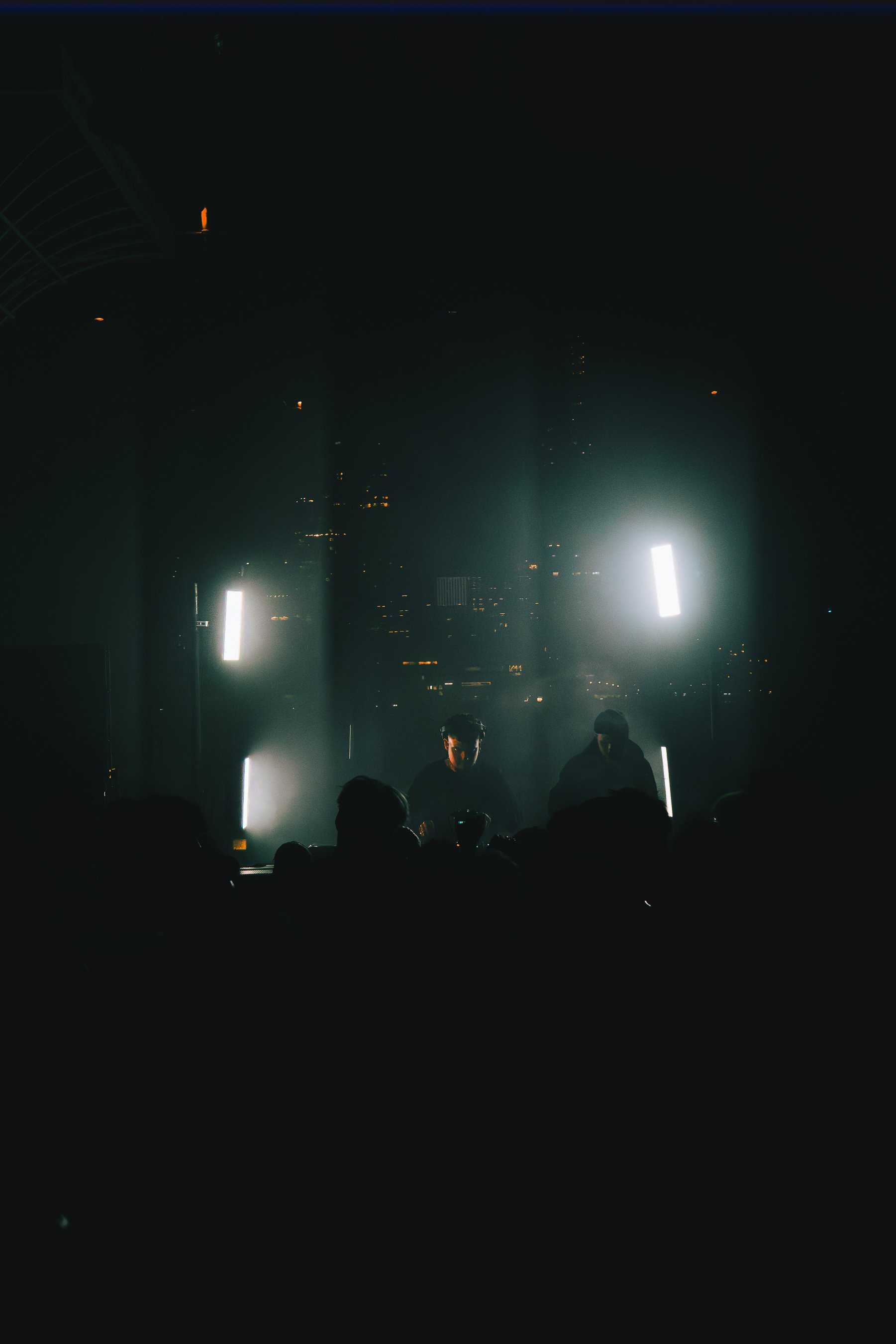 A dark indoor scene with silhouettes of people and bright vertical lights, possibly a stage with performers.
