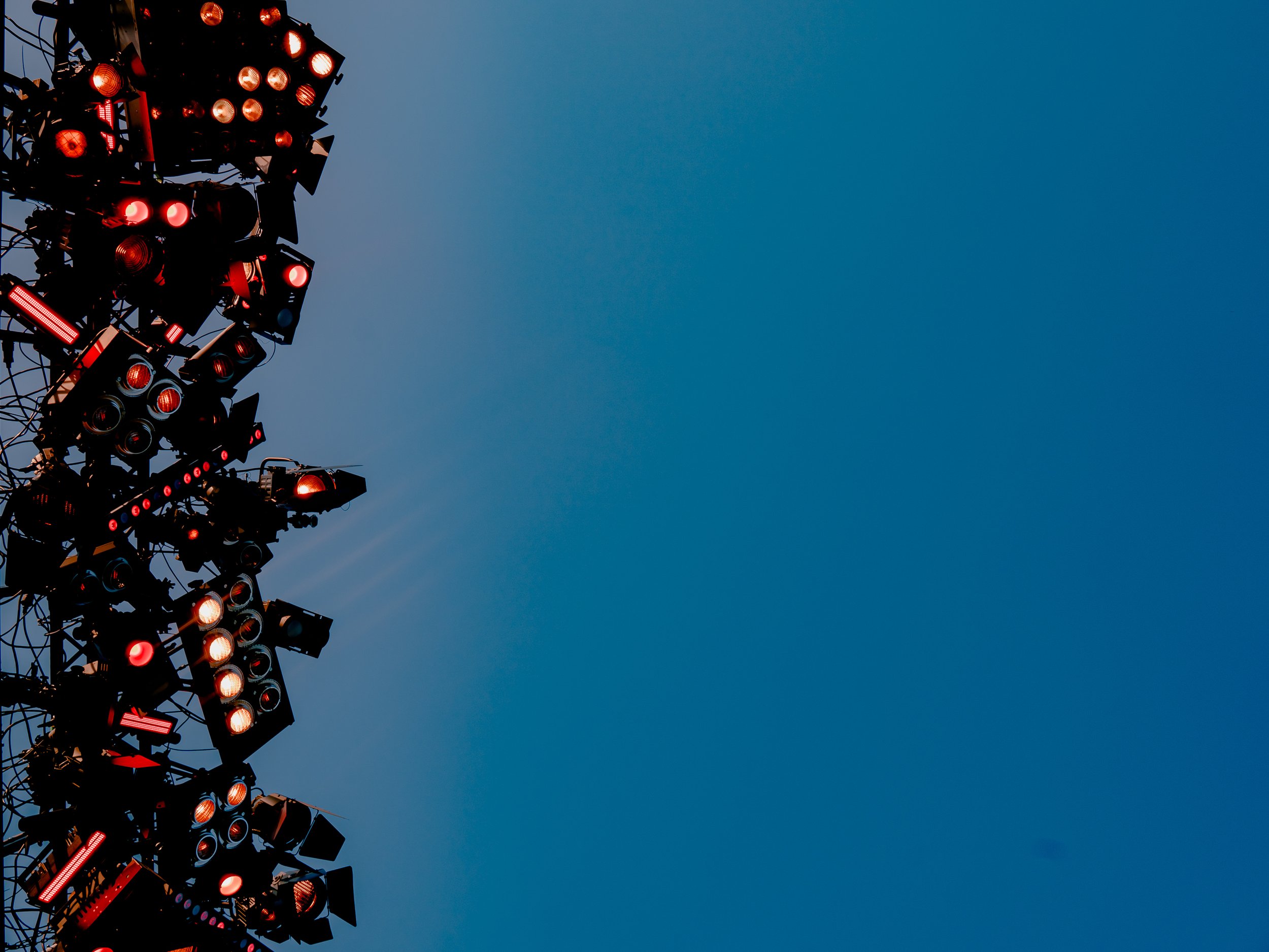 A tall structure with numerous red lights, possibly part of a stage or event lighting setup, against a clear blue sky.