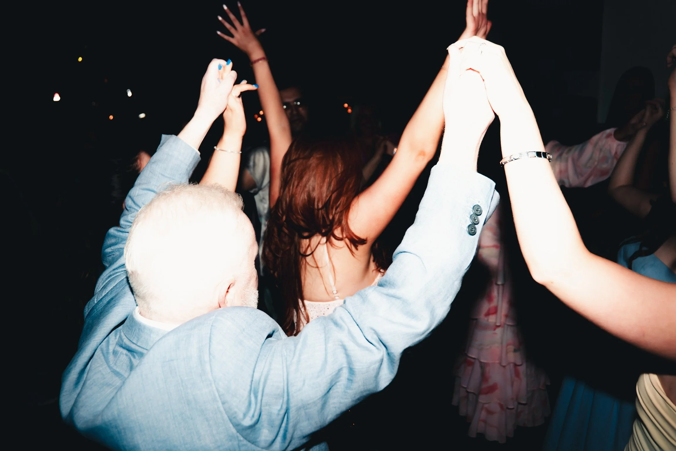 People dancing with their hands raised at a party or celebration in a dark environment.