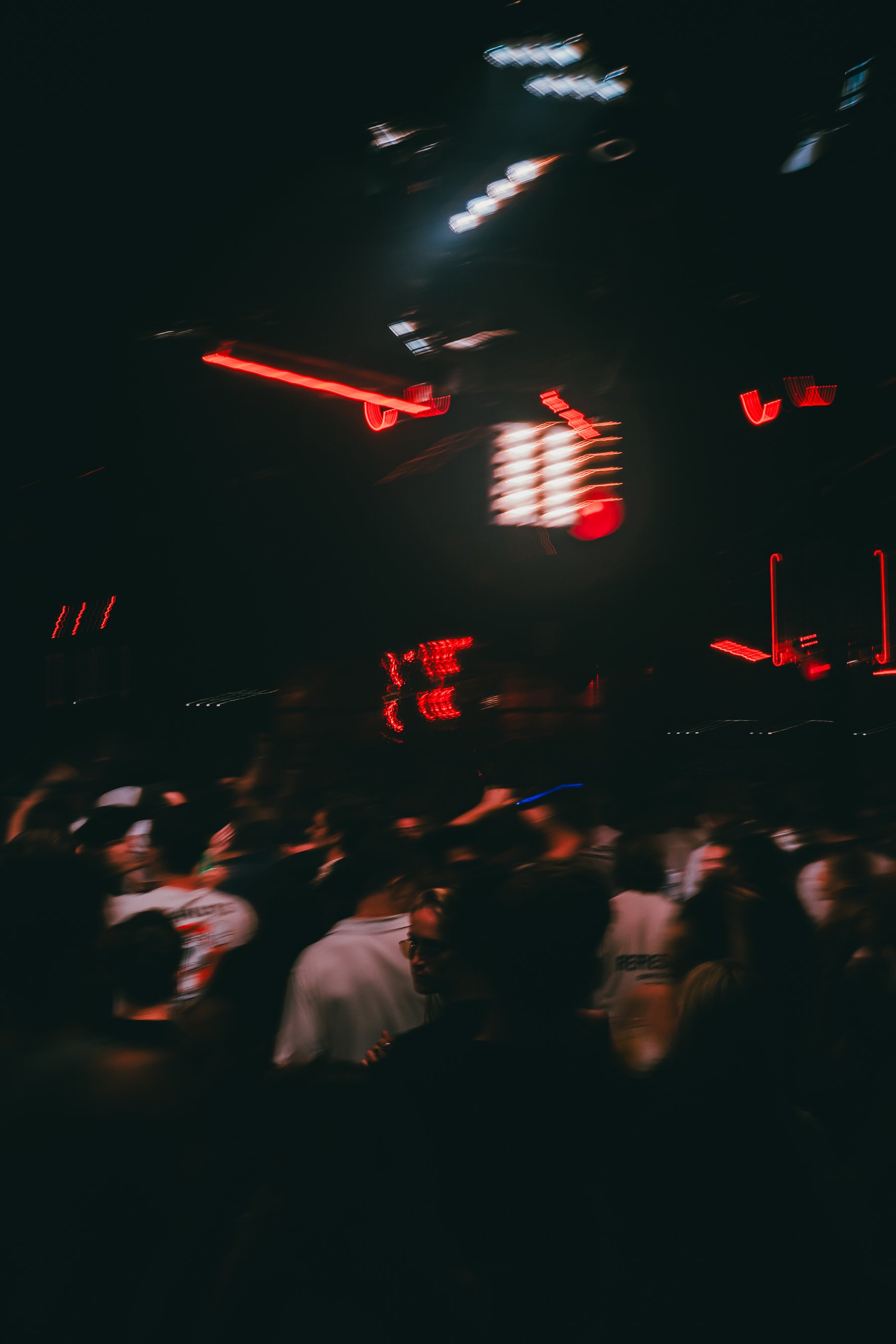 Nighttime scene with blurred cars and a crowd of people, possibly at an outdoor event or concert.