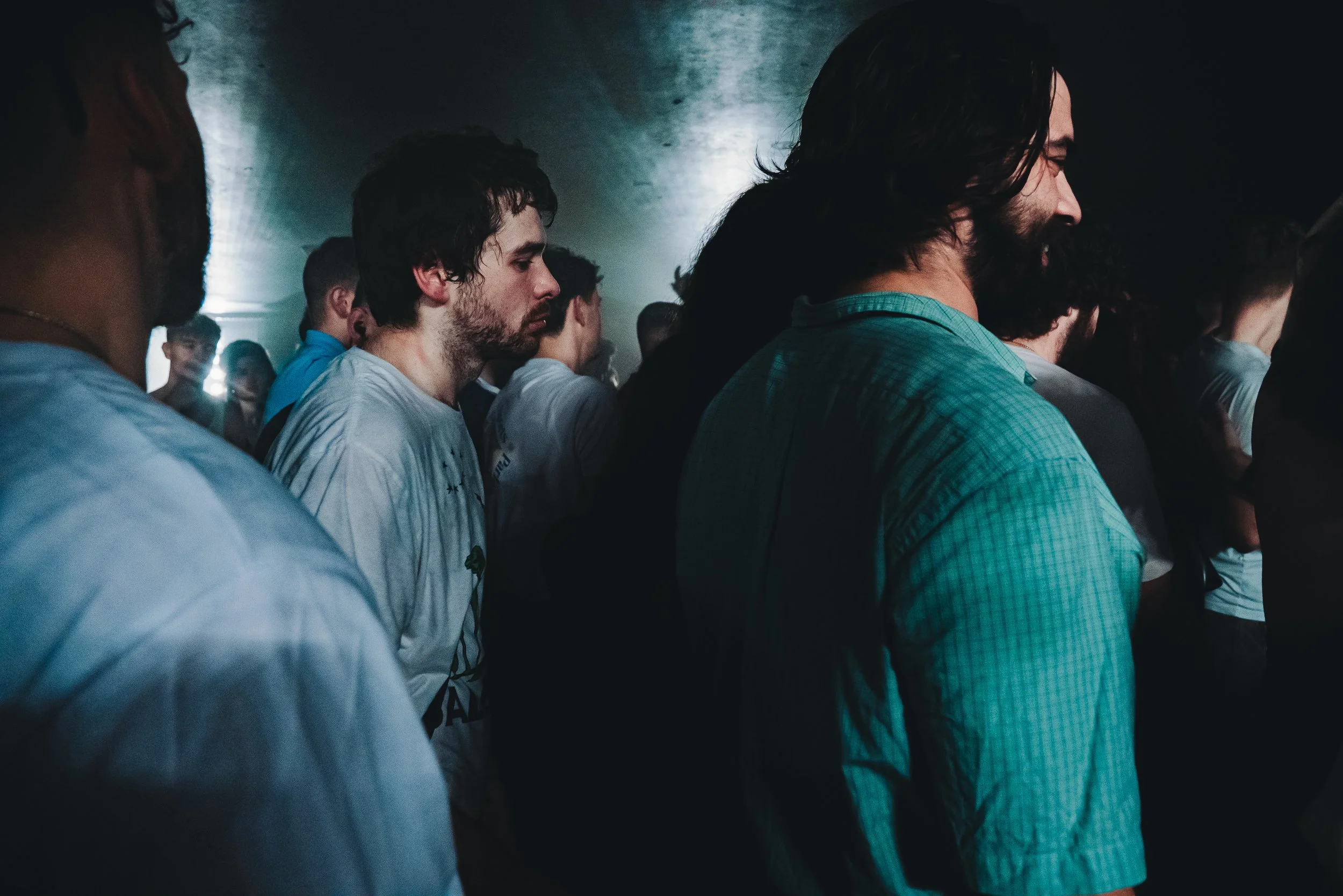 Group of people standing closely together in a dimly lit room, some with eyes closed, appearing to be meditating or praying.