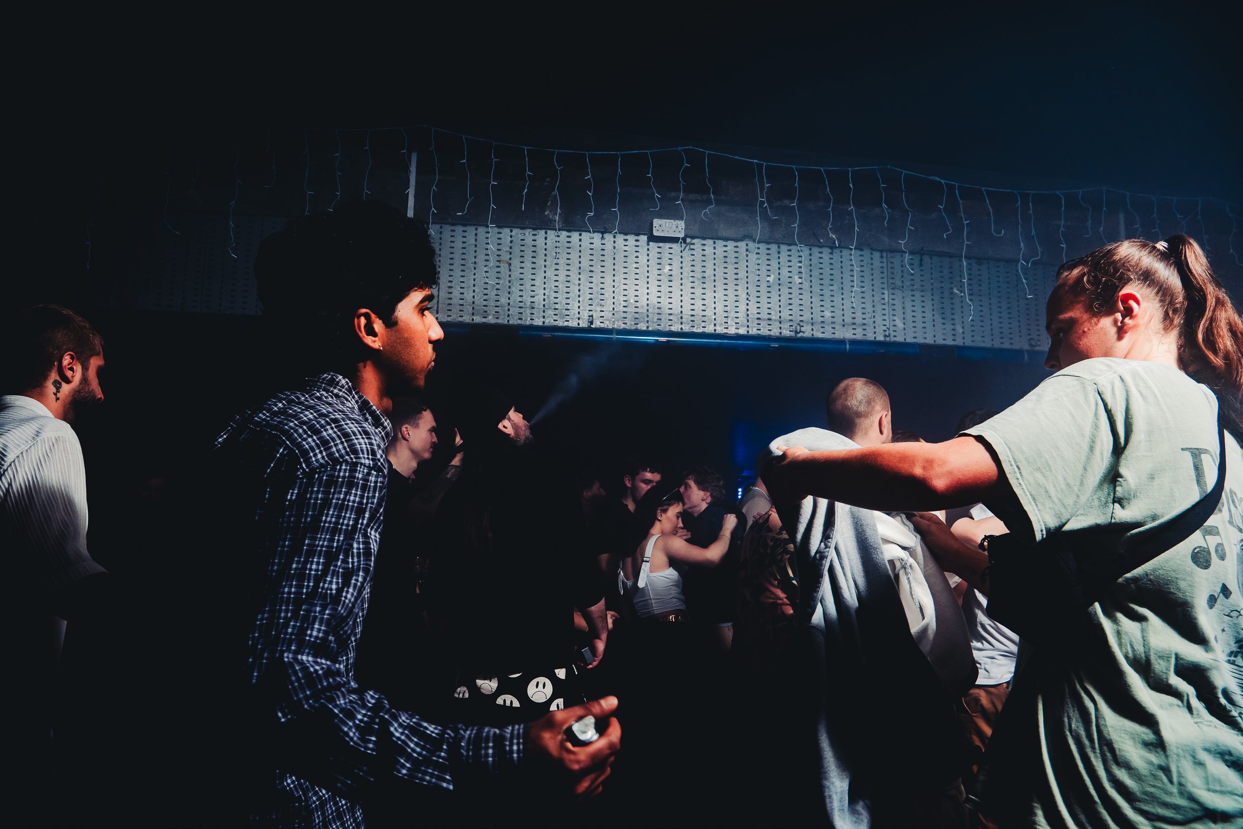 People dancing and socializing at a nightclub with dark lighting, some holding drinks, with string lights hanging from the ceiling.