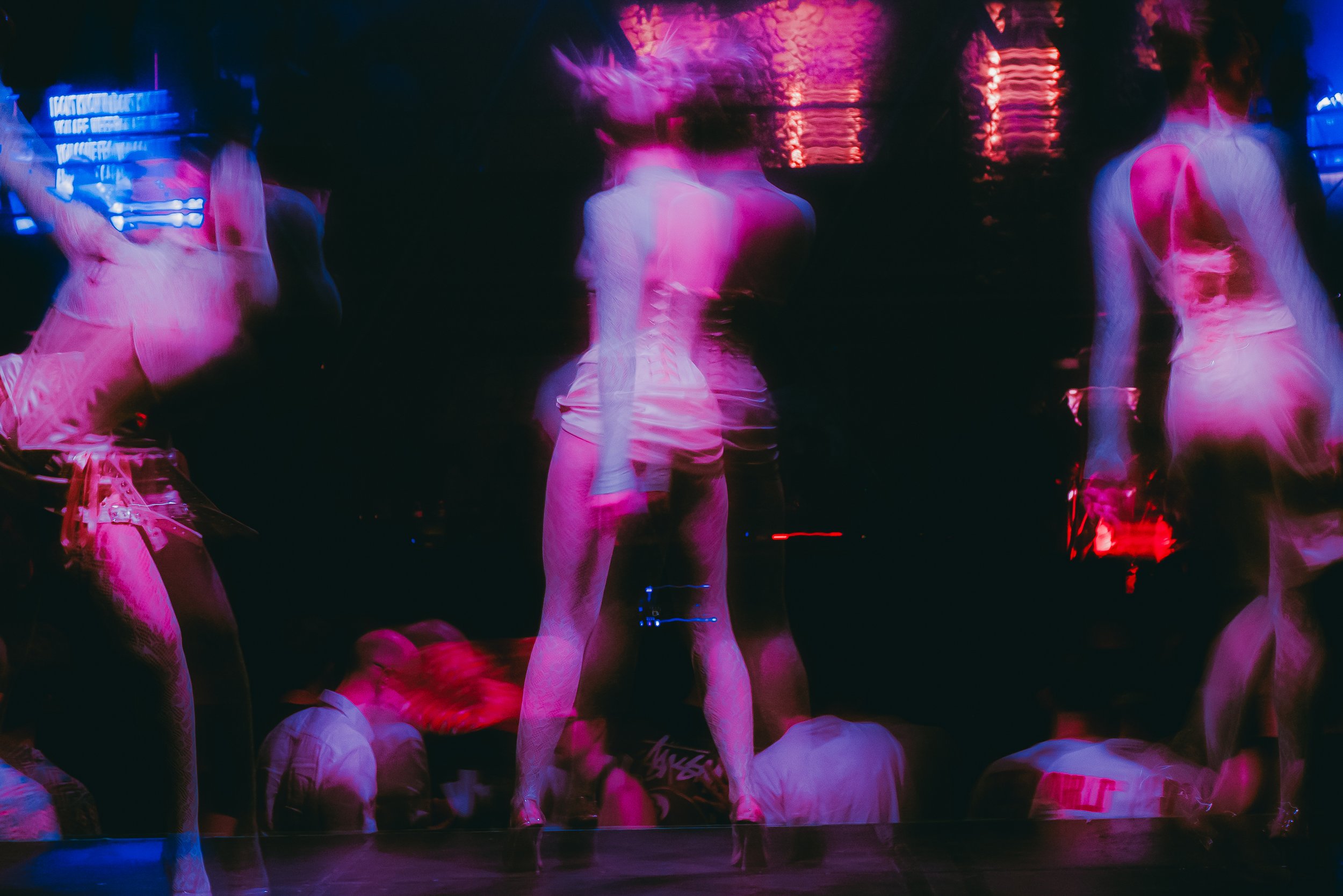 People at a nightclub dancing under pink and purple neon lights with blurred motion.