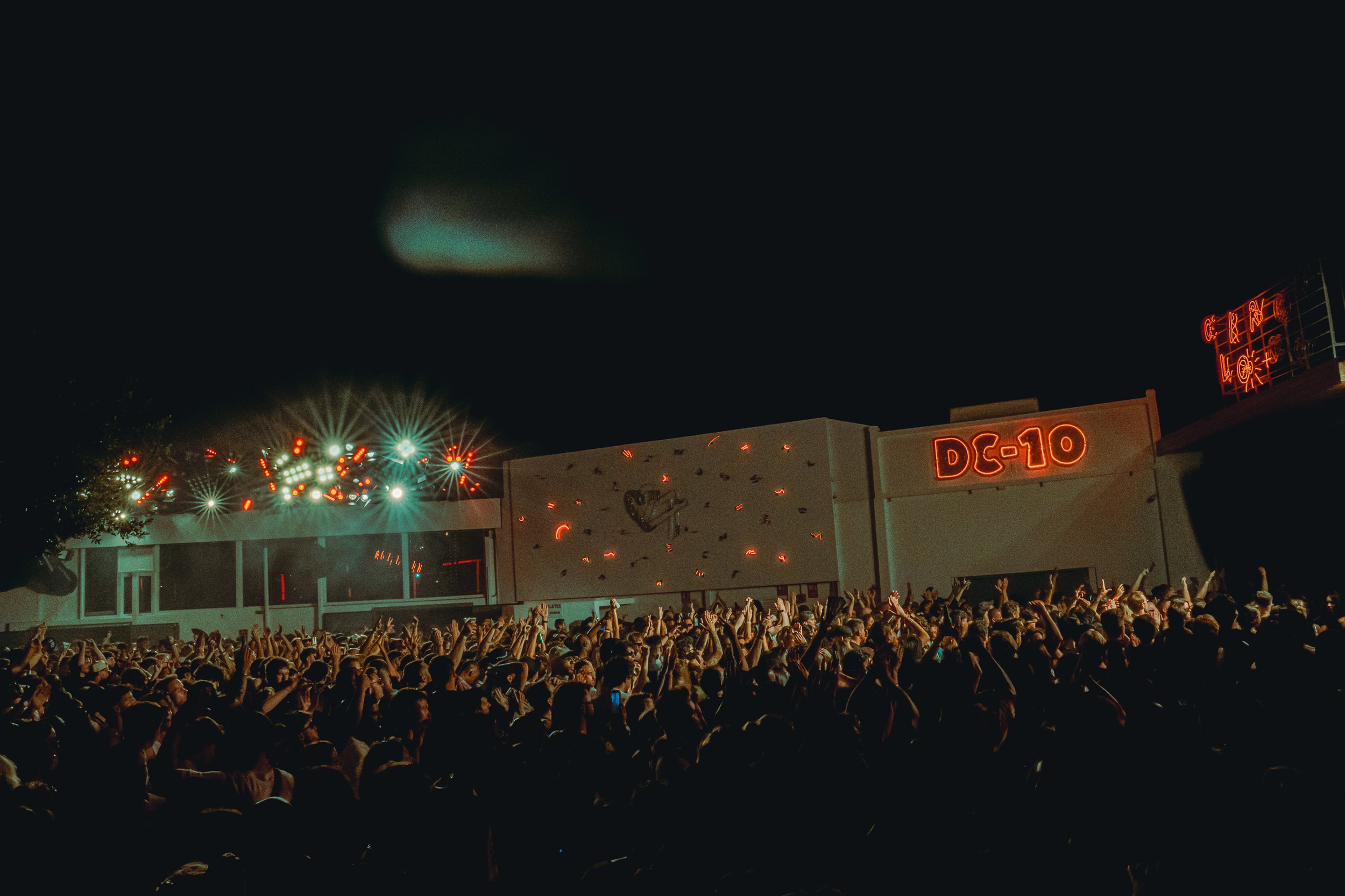 Crowd attending a concert or festival at night with stage lights and neon signs in the background.