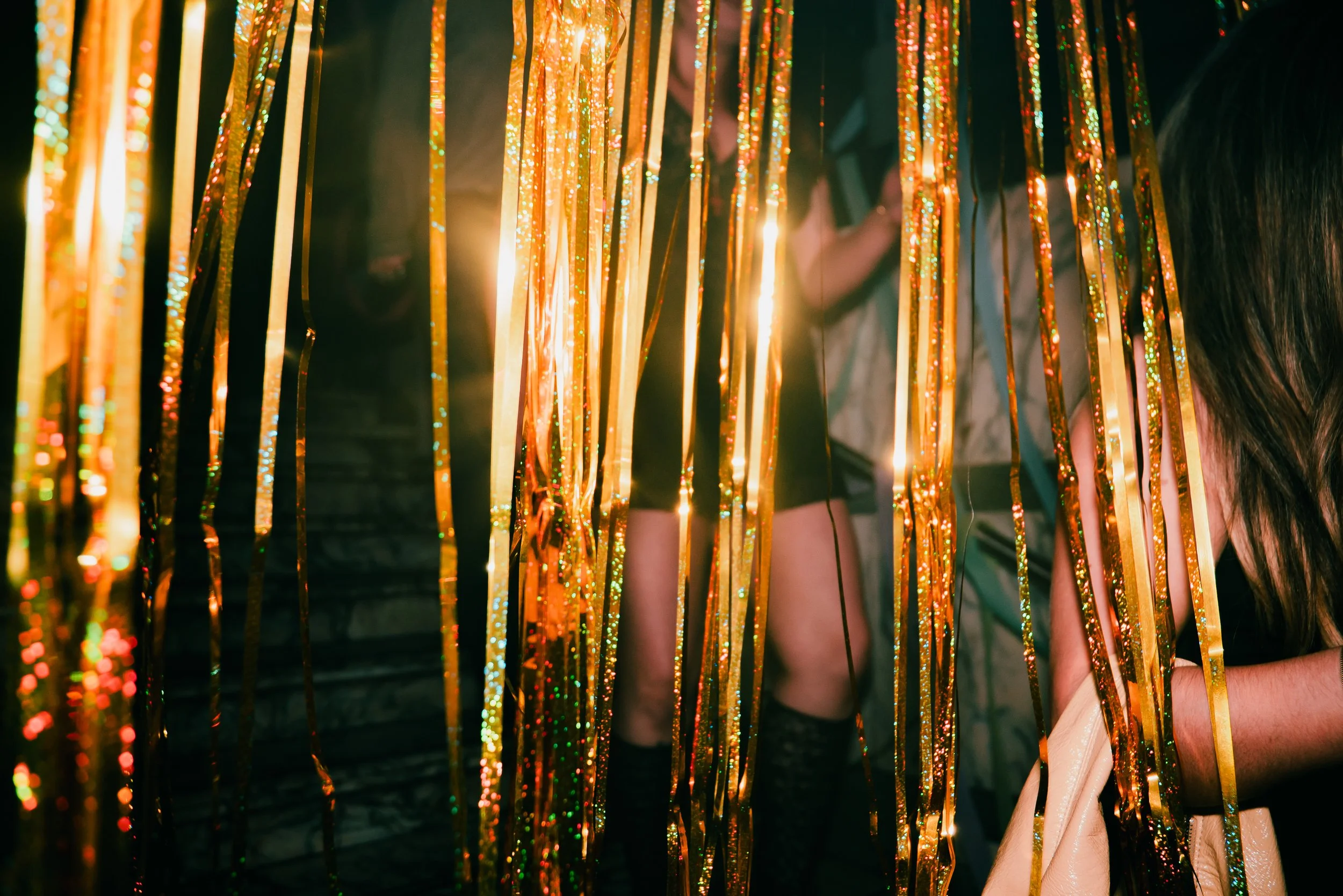 People behind shiny gold and orange streamers at an event.