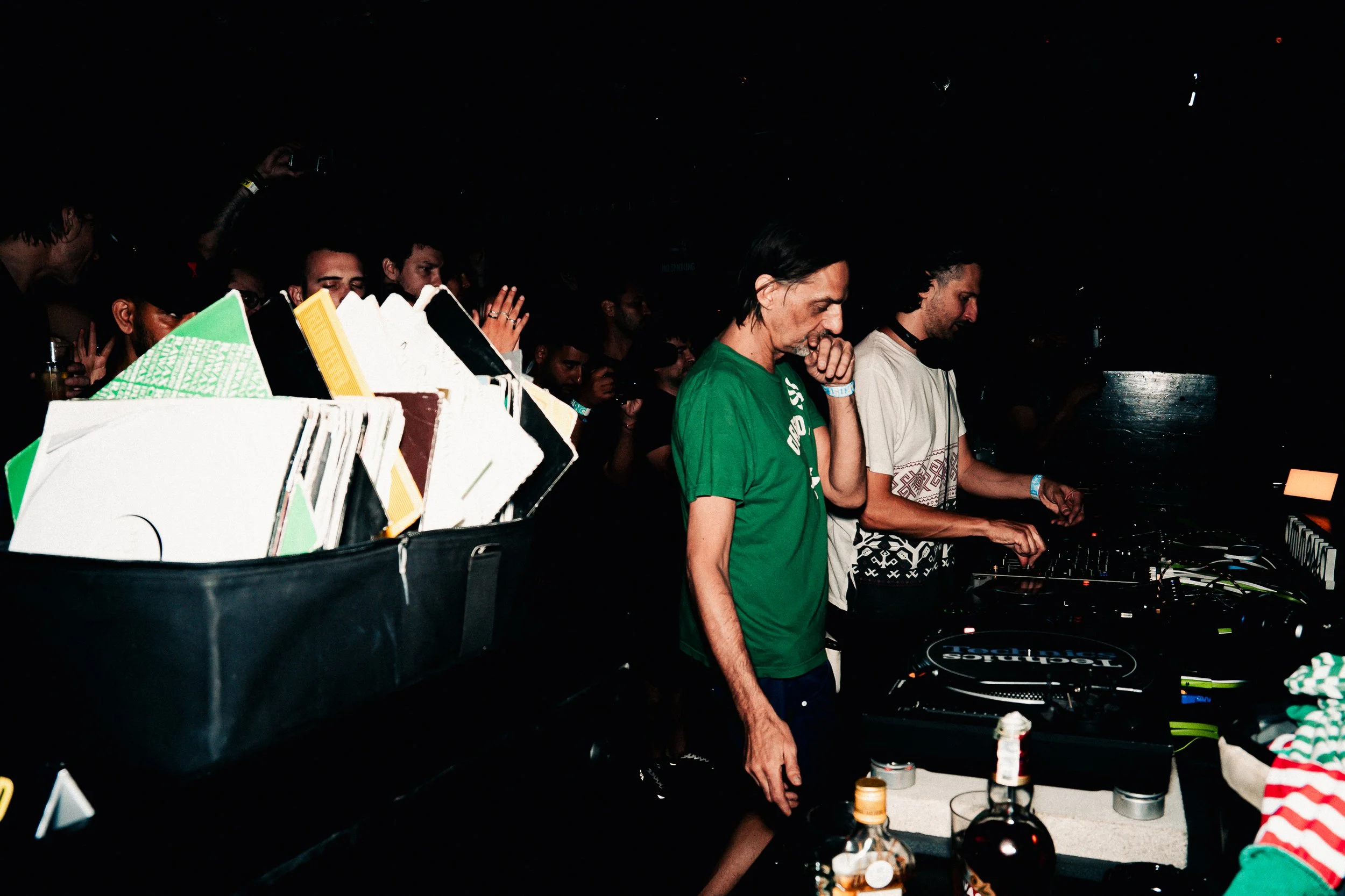 A group of people are DJing at a dark party or event, with some focused on equipment and others enjoying the music.