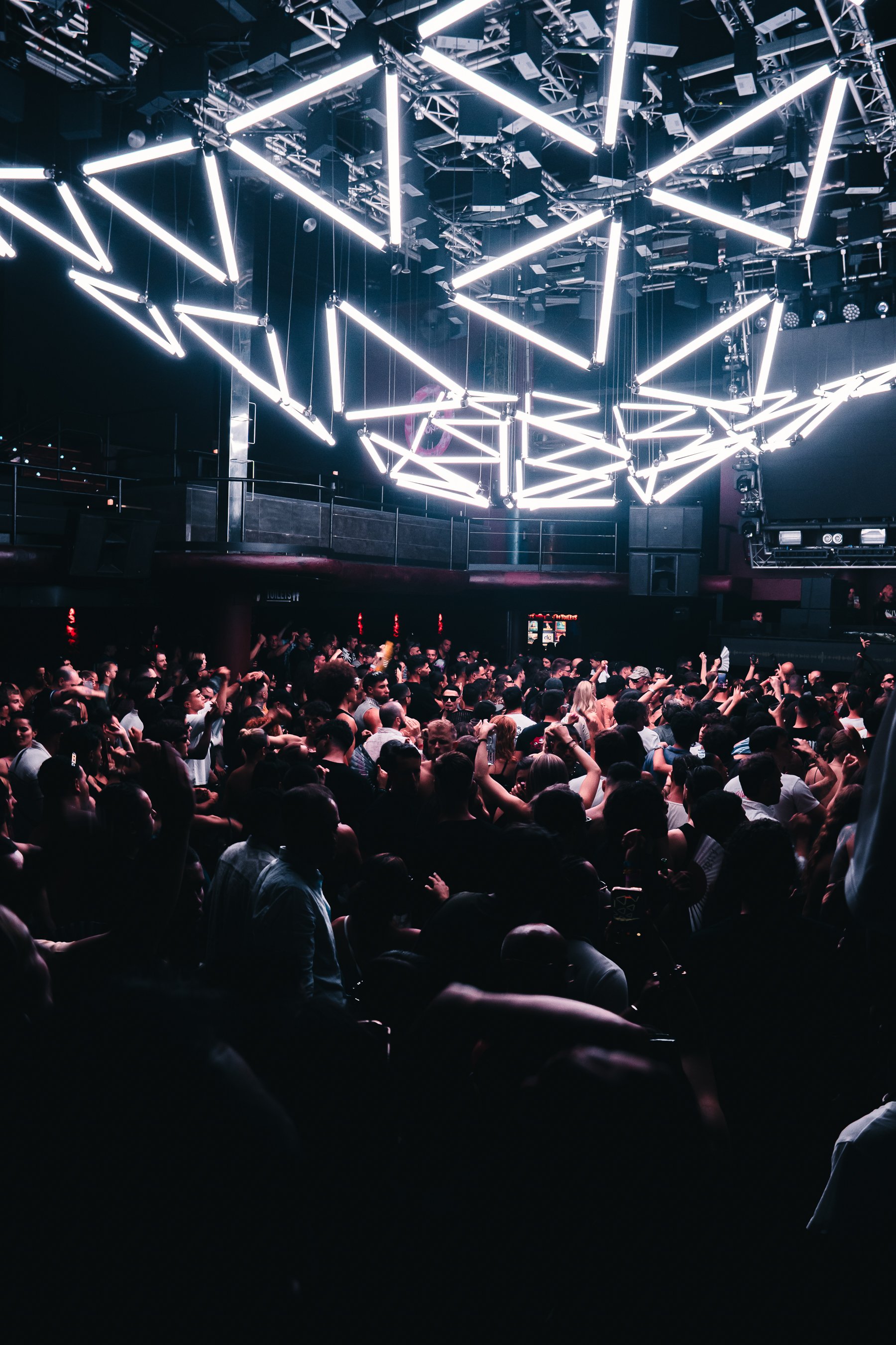 Crowd of people at a concert or nightclub with modern geometric light fixtures overhead.