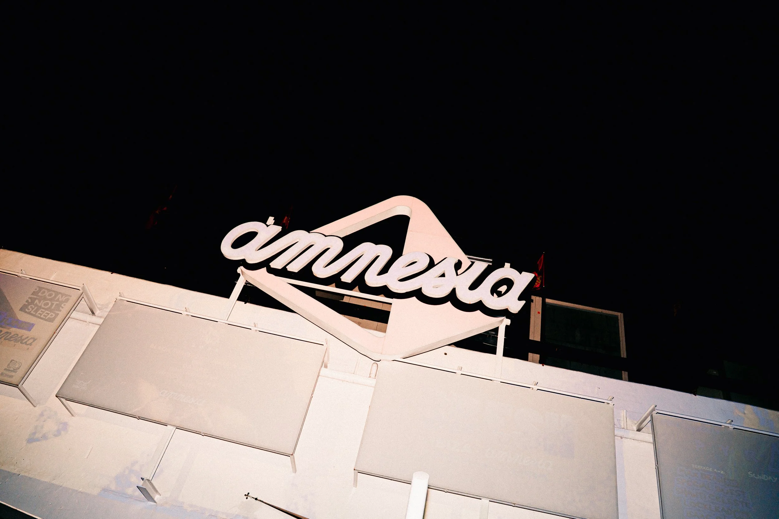 Nighttime view of a building with a large illuminated sign that reads 'amc' in a cursive font, with dark sky in the background.