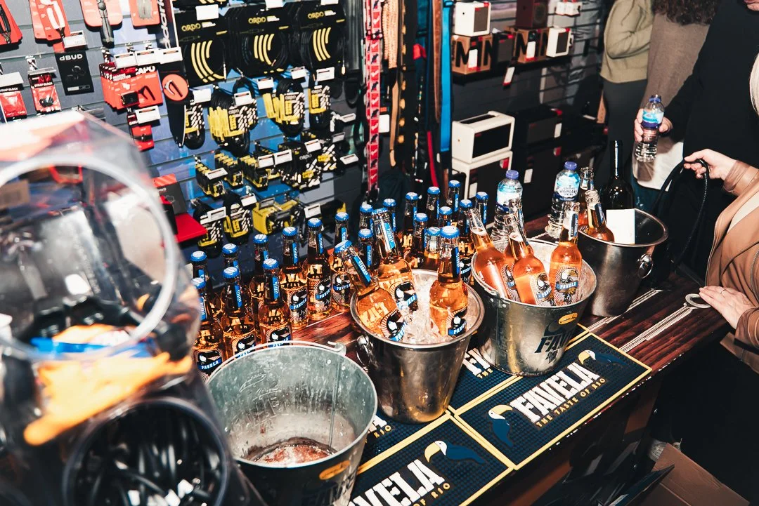 Cold bottles of Modelo beer in ice buckets on a bar counter, with people holding water bottles nearby, in a retail store setting.