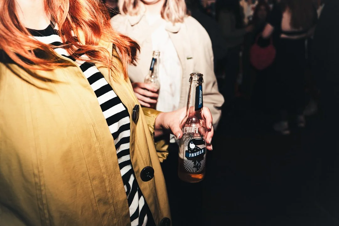 Person holding a glass bottle of beer or soda at a social gathering or party.