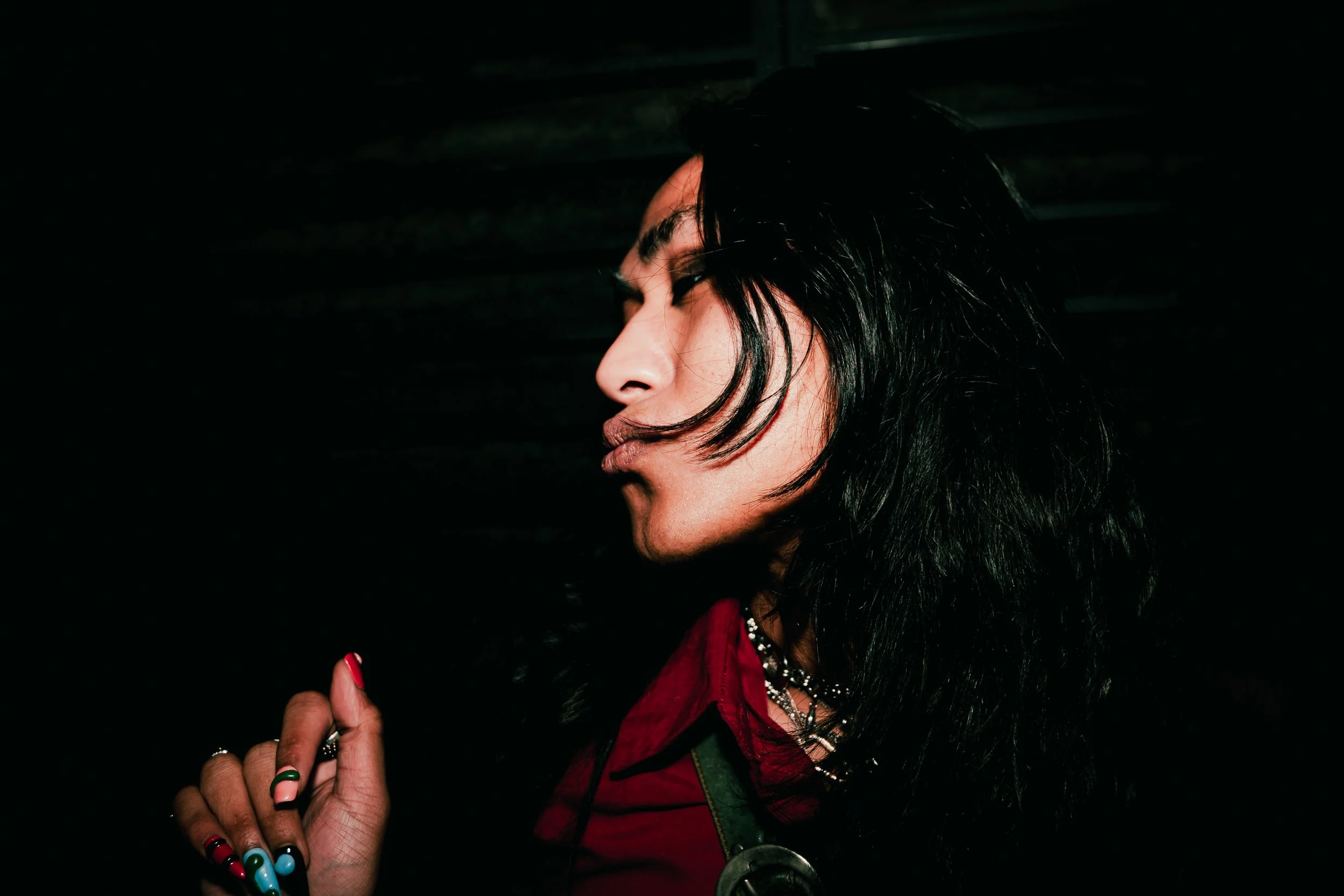 A woman with dark hair, wearing multiple necklaces and a red jacket, is looking at a smartphone in her hand.
