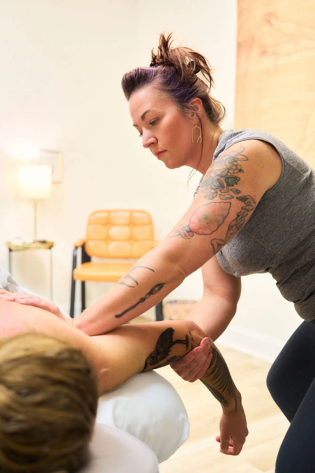 A female massage therapist providing massage to a woman on a treatment table in an office setting.