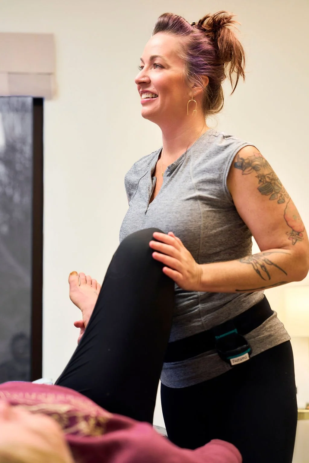 A female massage therapist smiling and holding a person's leg during a massage session.