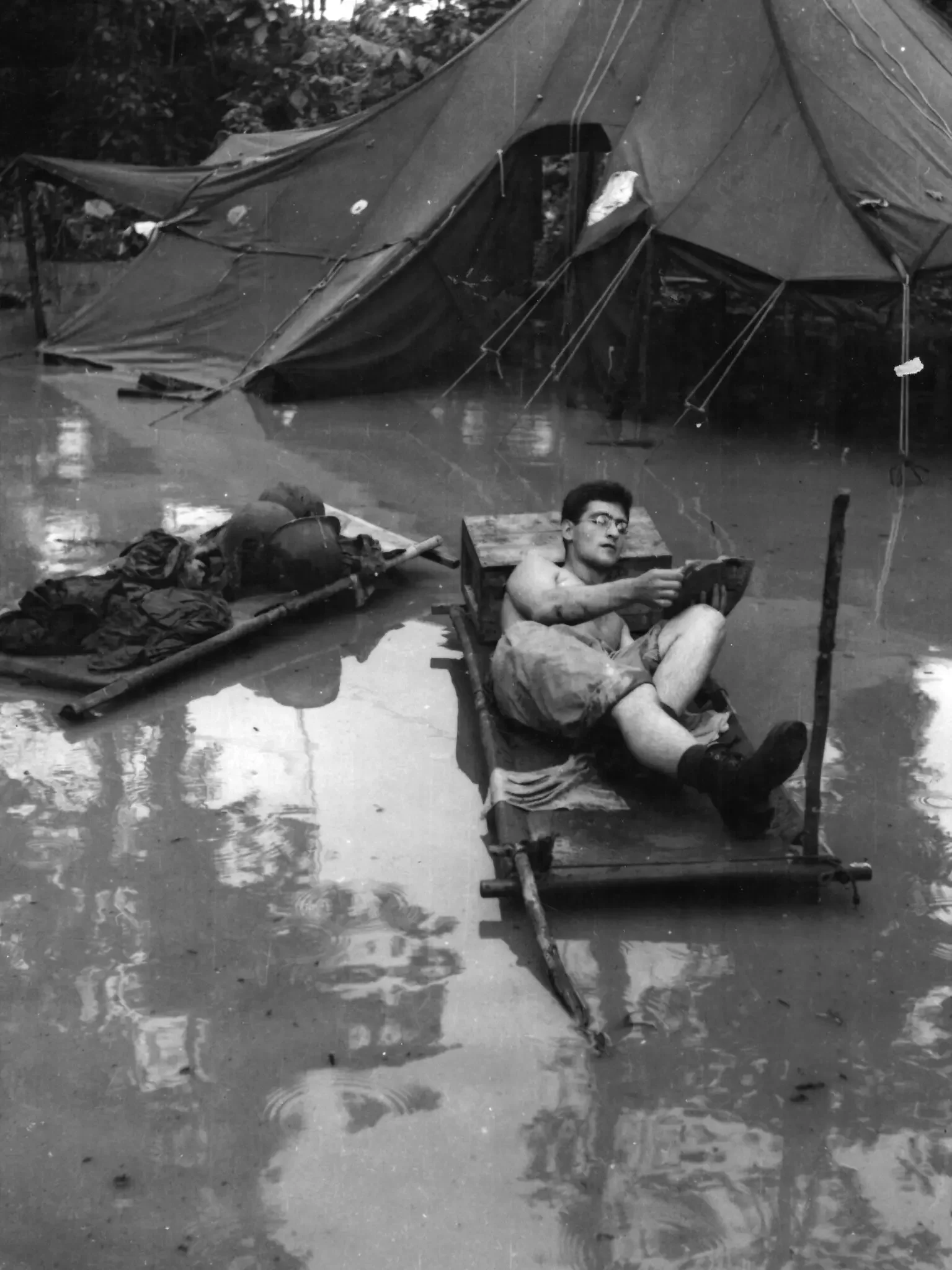 A soldier reading in a flooded camp in New Guinea during World War II