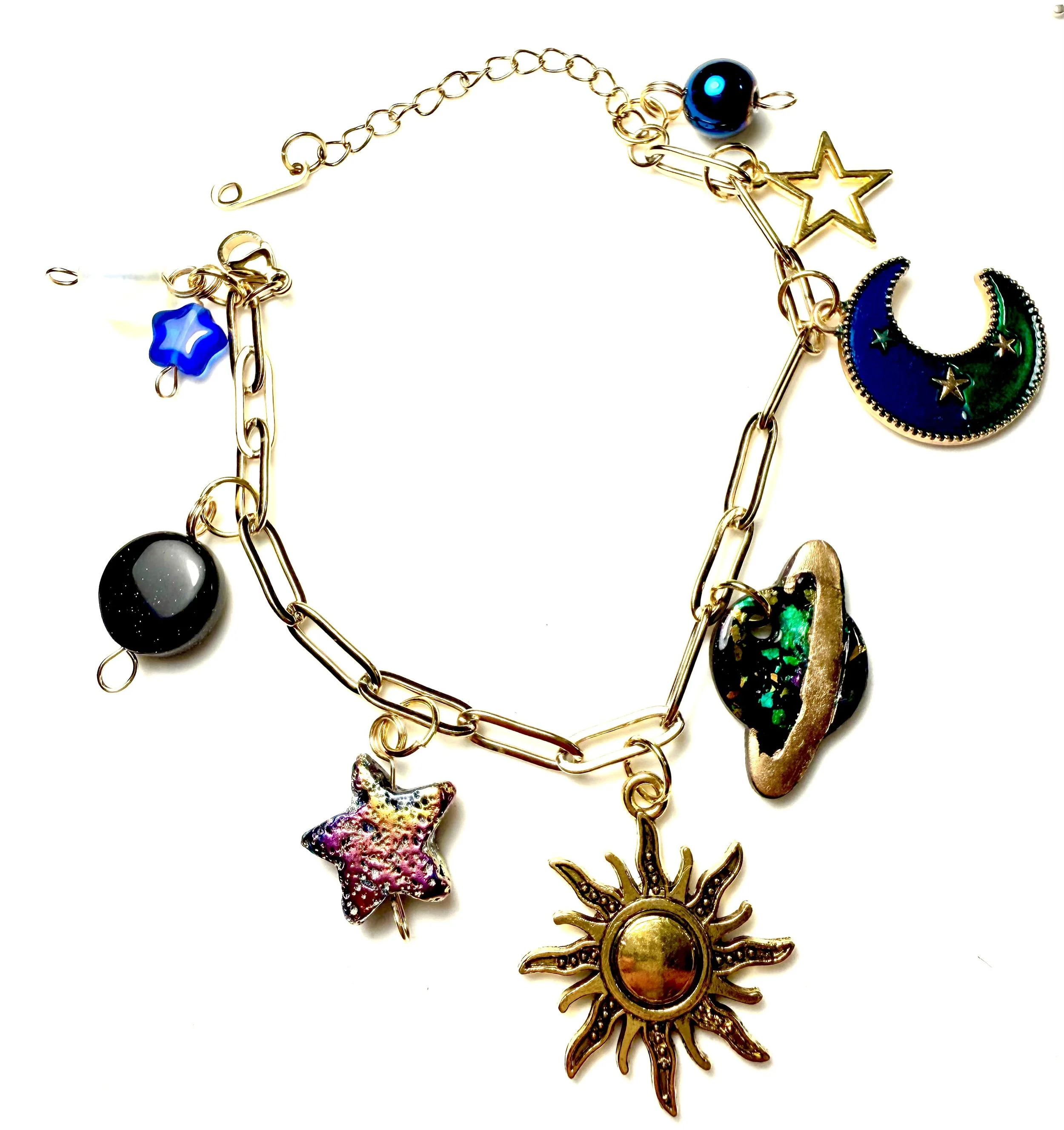 Collection of colorful jewelry charms including a sun, moon, star, heart, and planet, connected by gold chains.