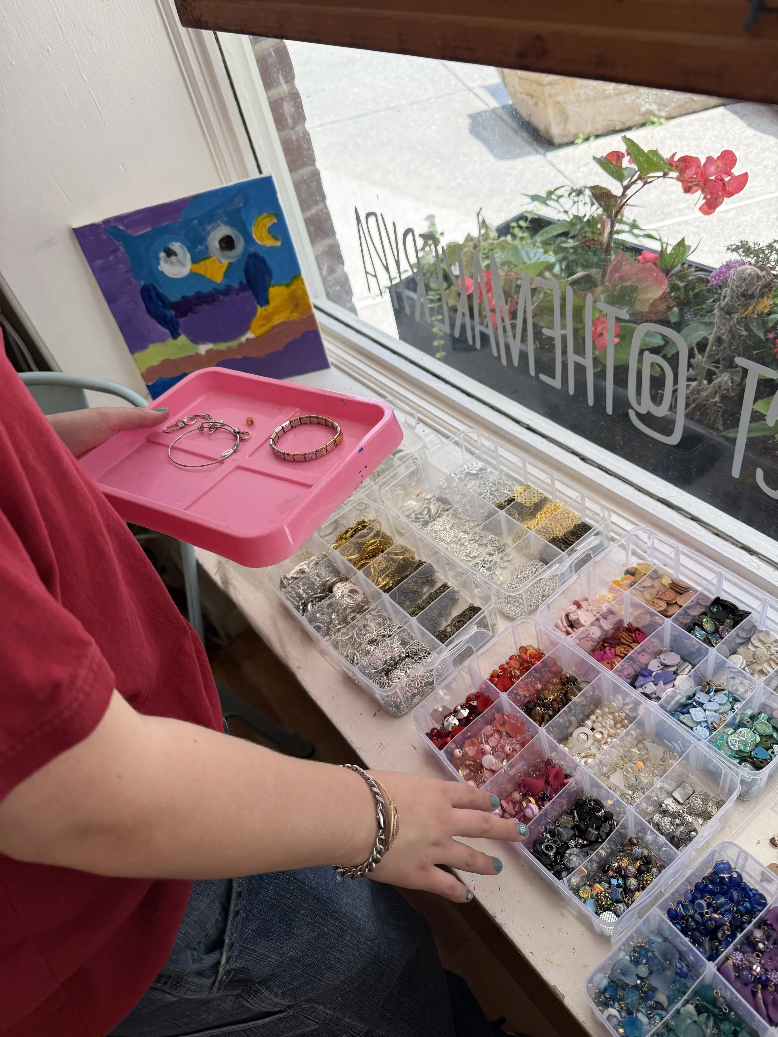 Person selecting from colorful beads and jewelry supplies in containers on a windowsill.