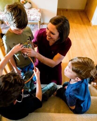 A woman and three children gathered around a staircase, with the woman helping one of the children put on a device, possibly a medical or assistive device.