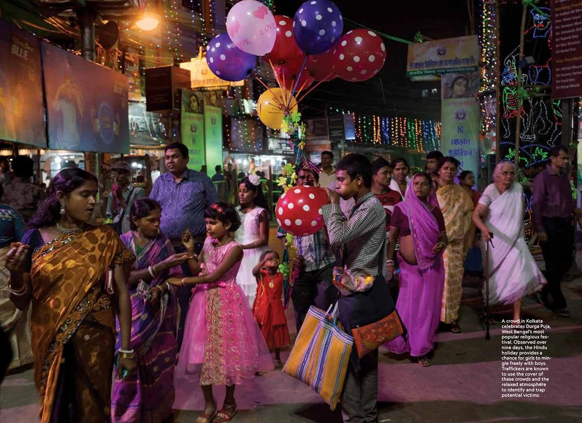 Crowd celebrating, decorated with colorful lights and balloons, with women in sarees and children, at night.