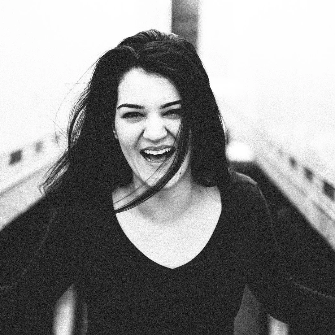 A woman with dark hair laughing or smiling, wearing a dark top, in a black and white photo.